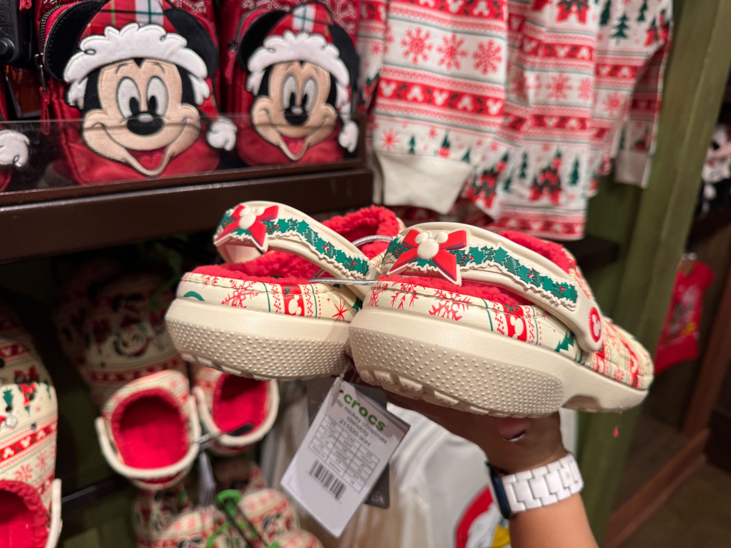 Hand holding festive holiday Crocs with red, green, and white Christmas patterns among Walt Disney World 2025 merchandise.
