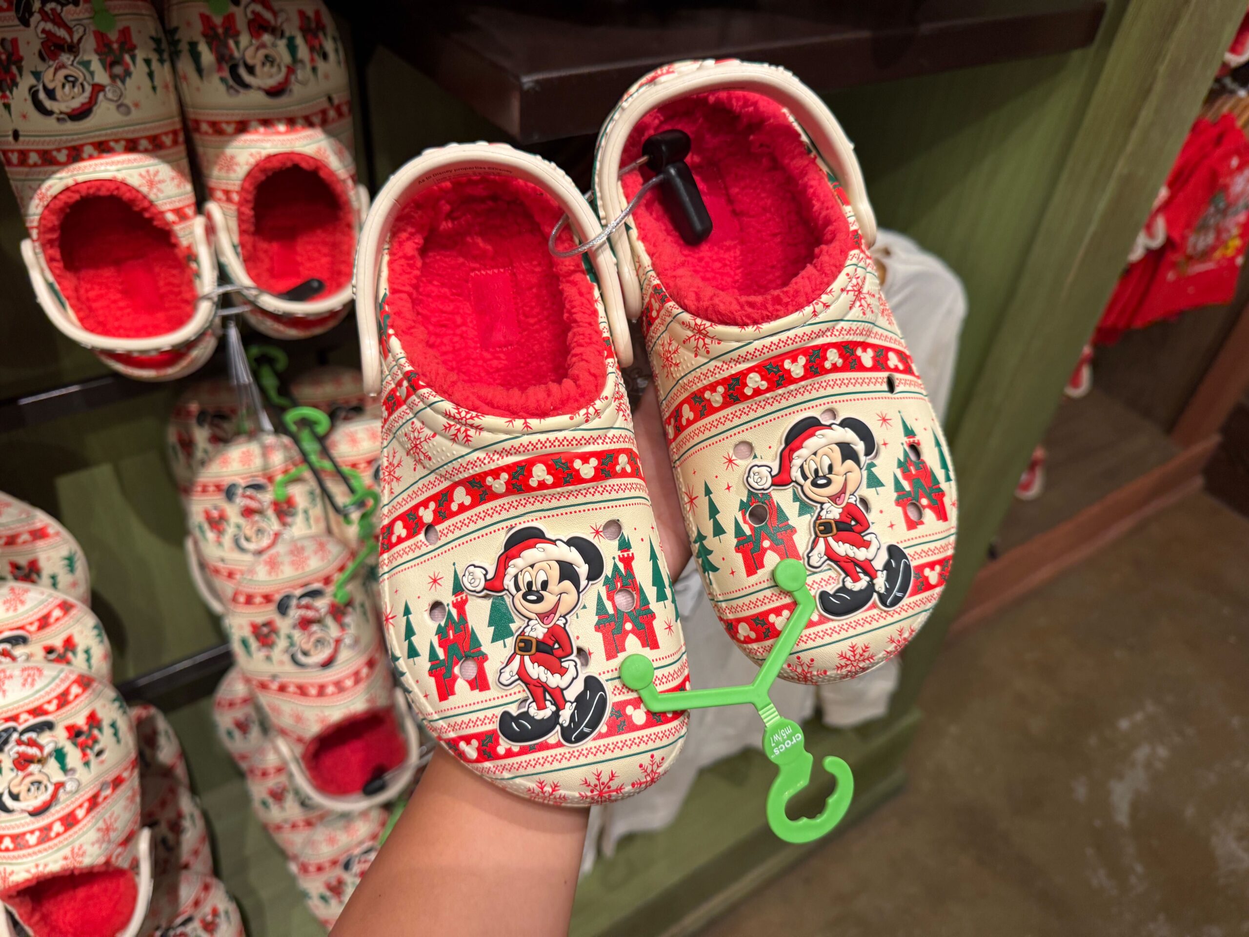 Hand holding festive Walt Disney World Christmas Merchandise Minnie Mouse slippers, red lining, in-store holiday display.