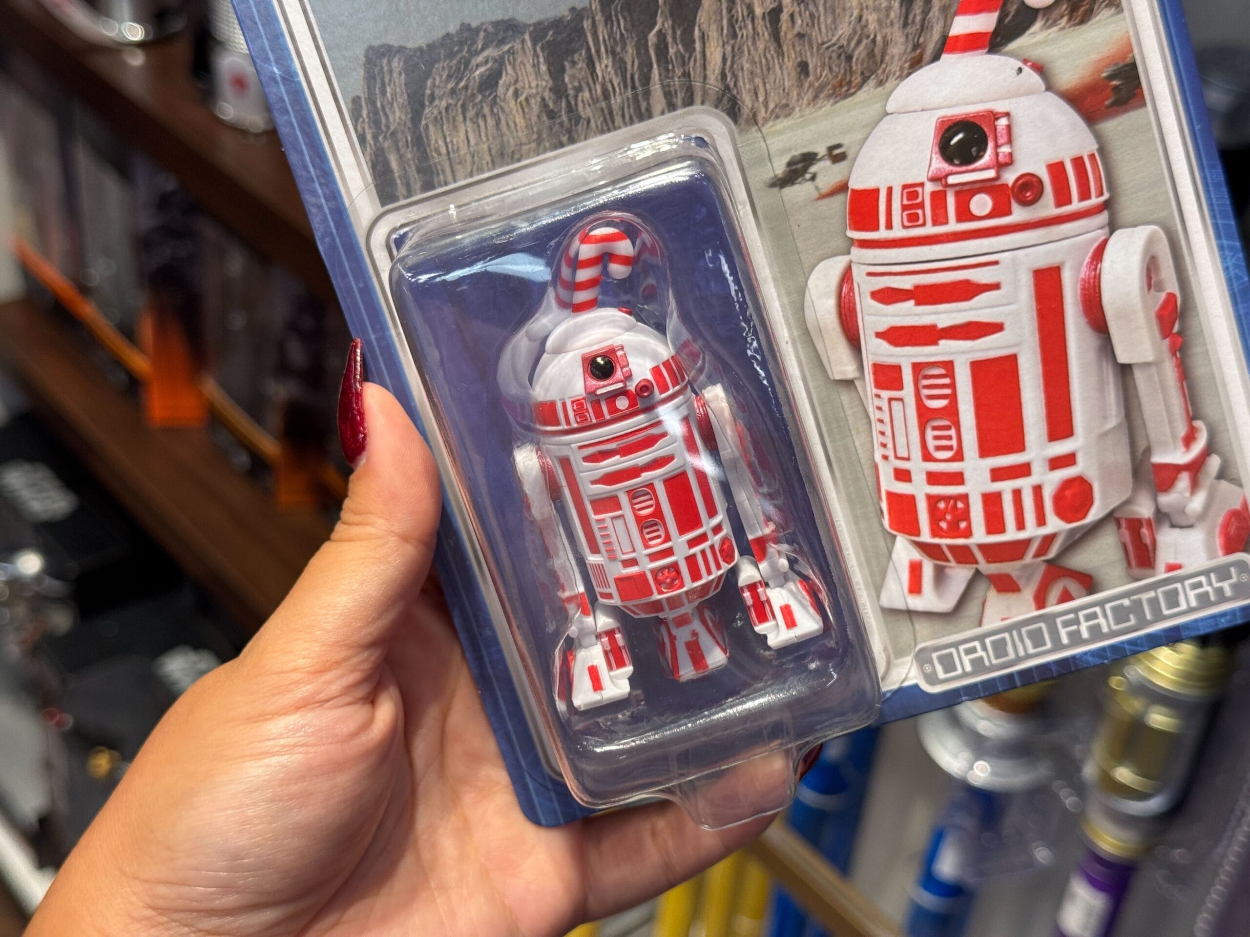 A hand holds a 2025 Christmas merchandise Star Wars droid toy from Walt Disney World labeled "Droid Factory.
