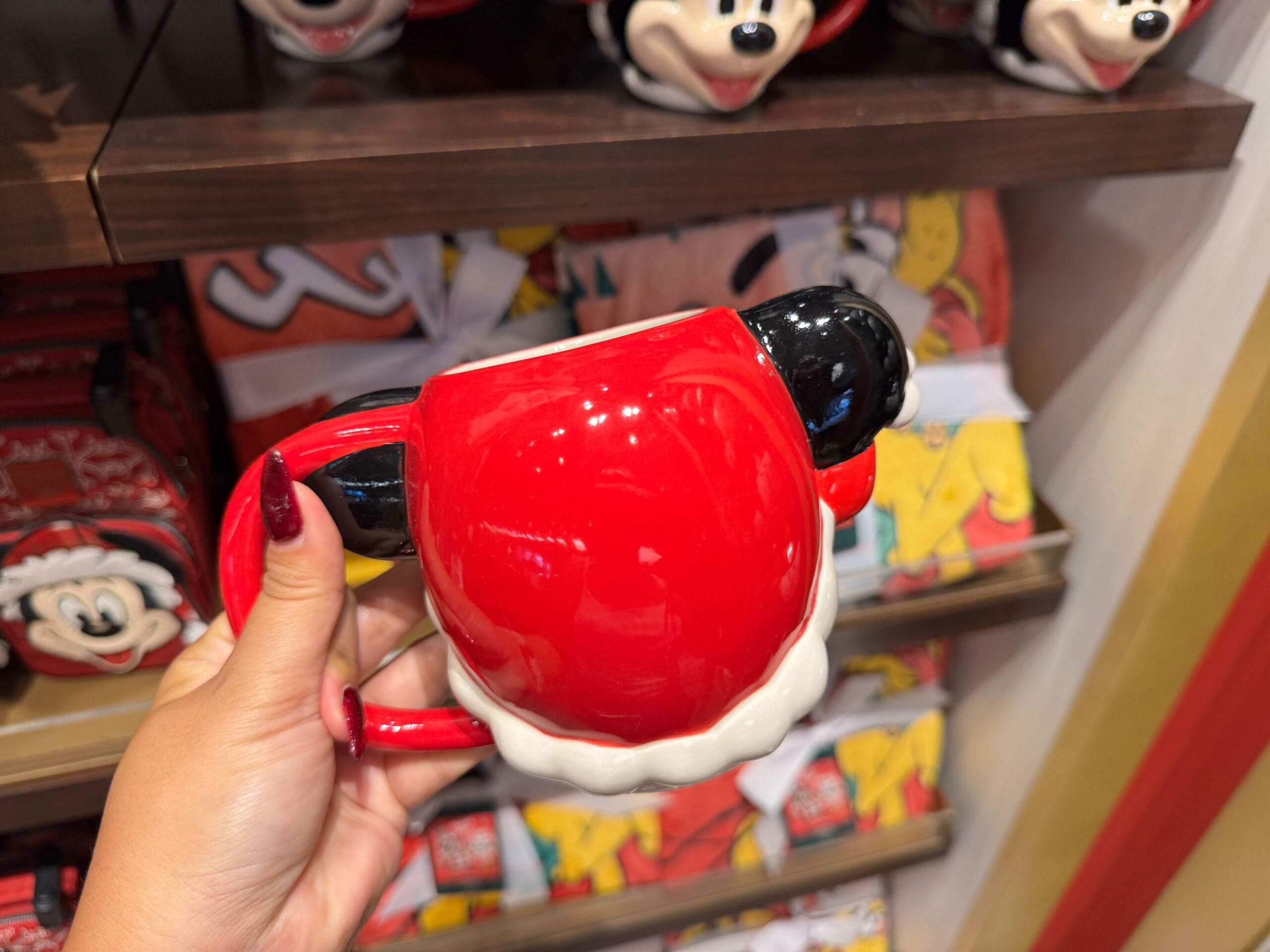 A hand holds a red Minnie Mouse mug among Disney World Christmas merchandise, with 2025 prices in the background.