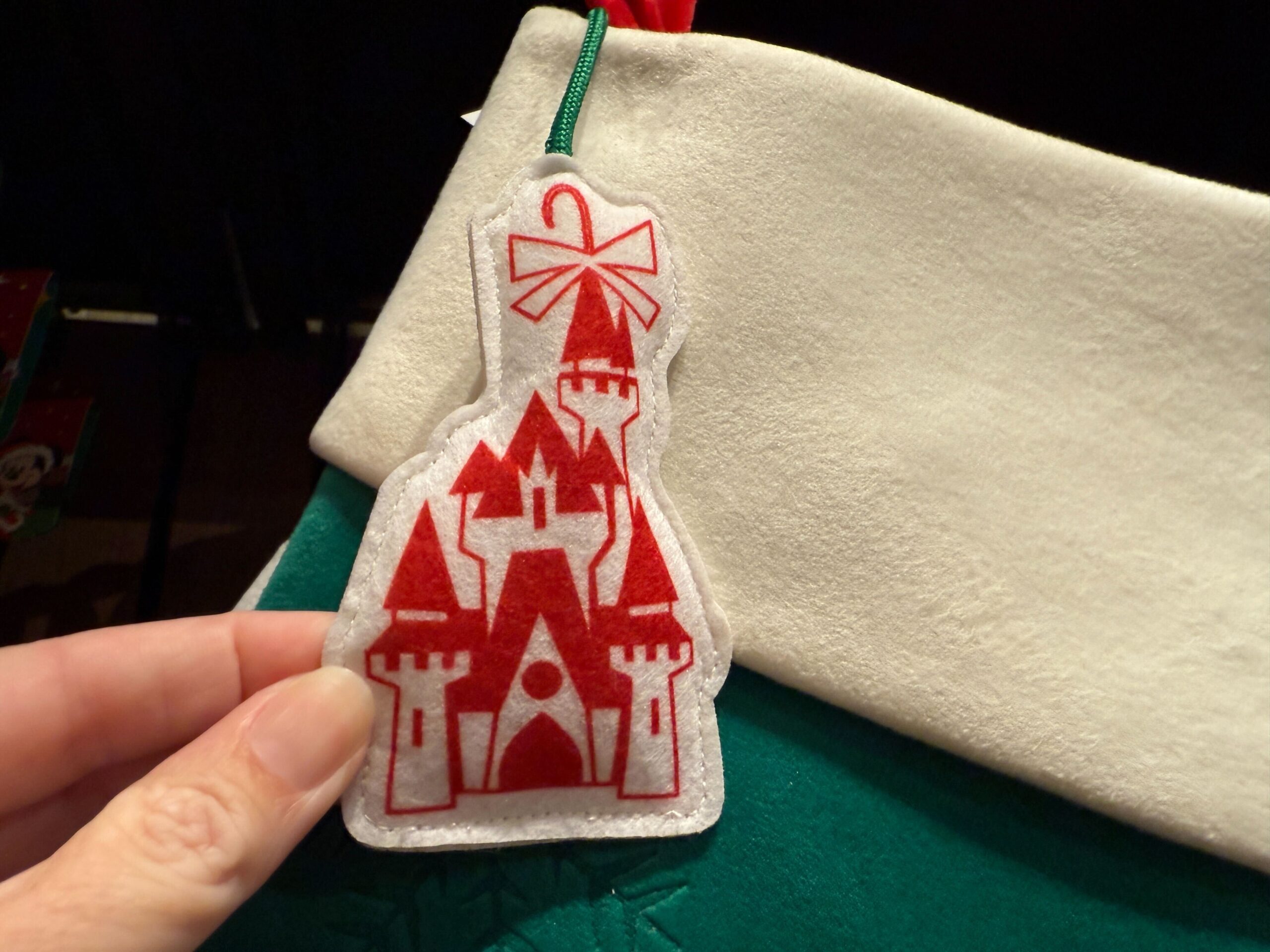 A hand holds a Walt Disney World red castle felt ornament with a bow, attached to a green and white Christmas stocking.