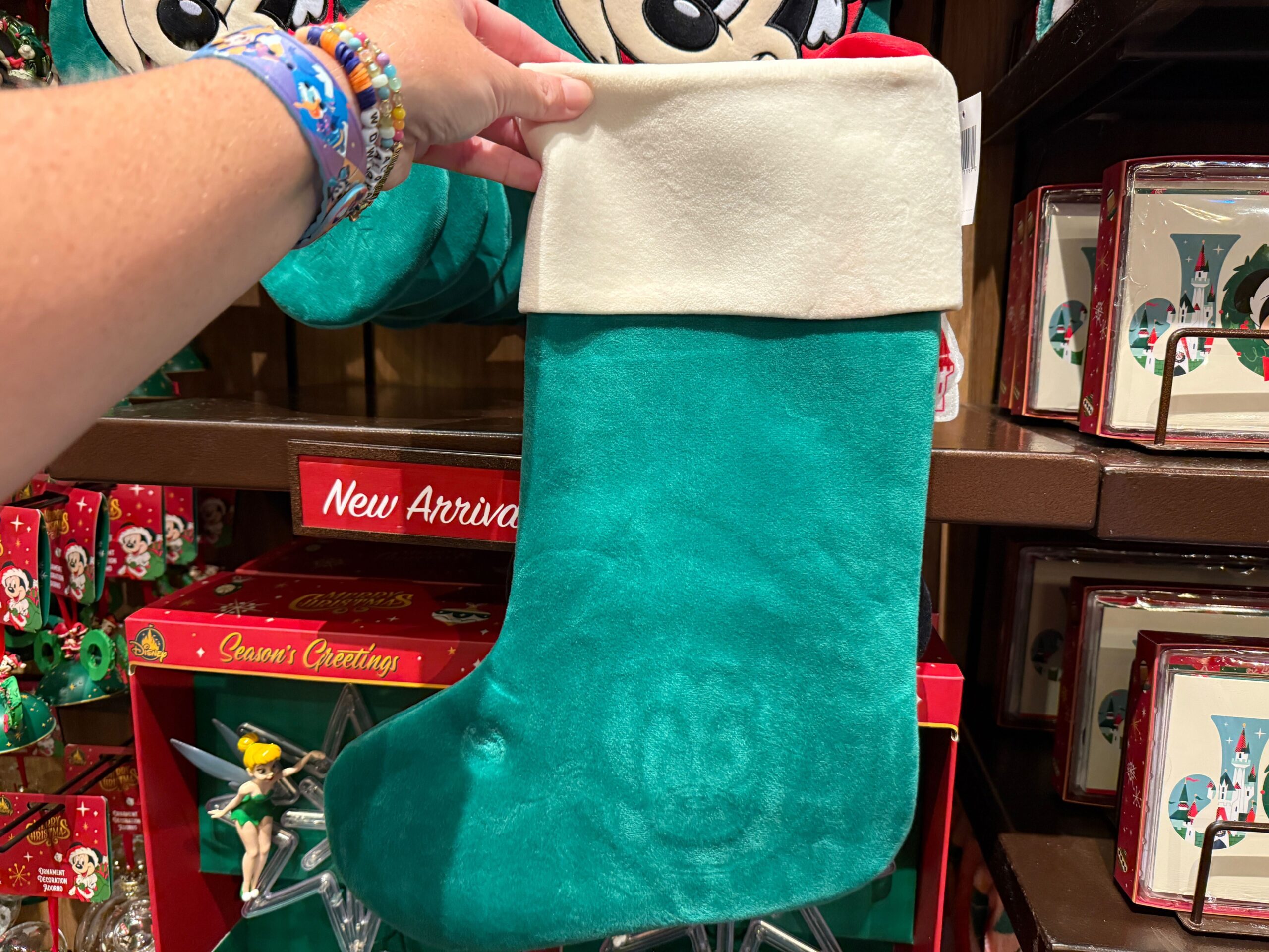 A hand holds a teal Christmas stocking with a white cuff from the 2025 Walt Disney World Christmas merchandise display.