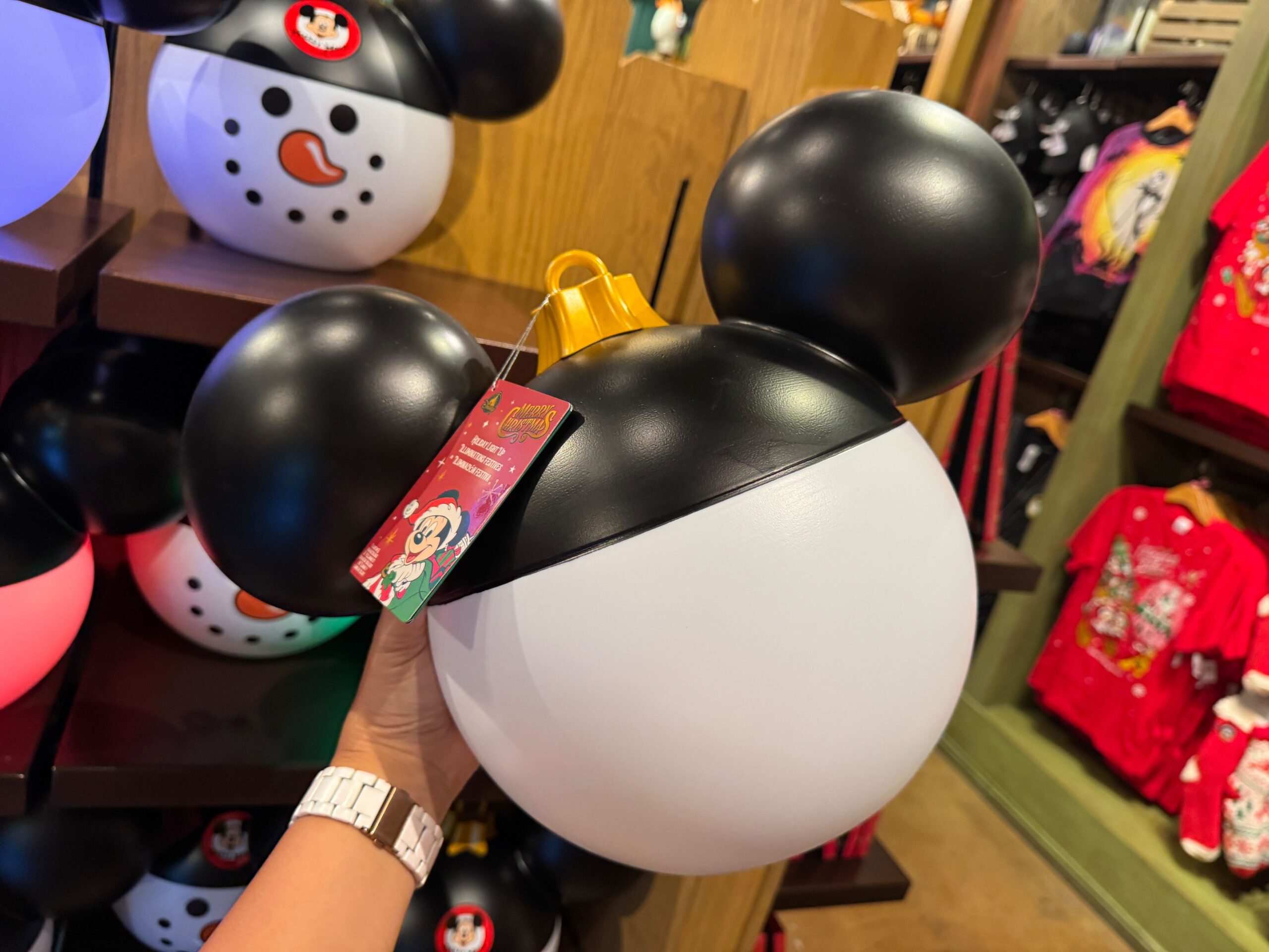 A hand holds a 2025 Mickey Mouse-shaped ornament, part of Walt Disney World's festive Christmas merchandise display.