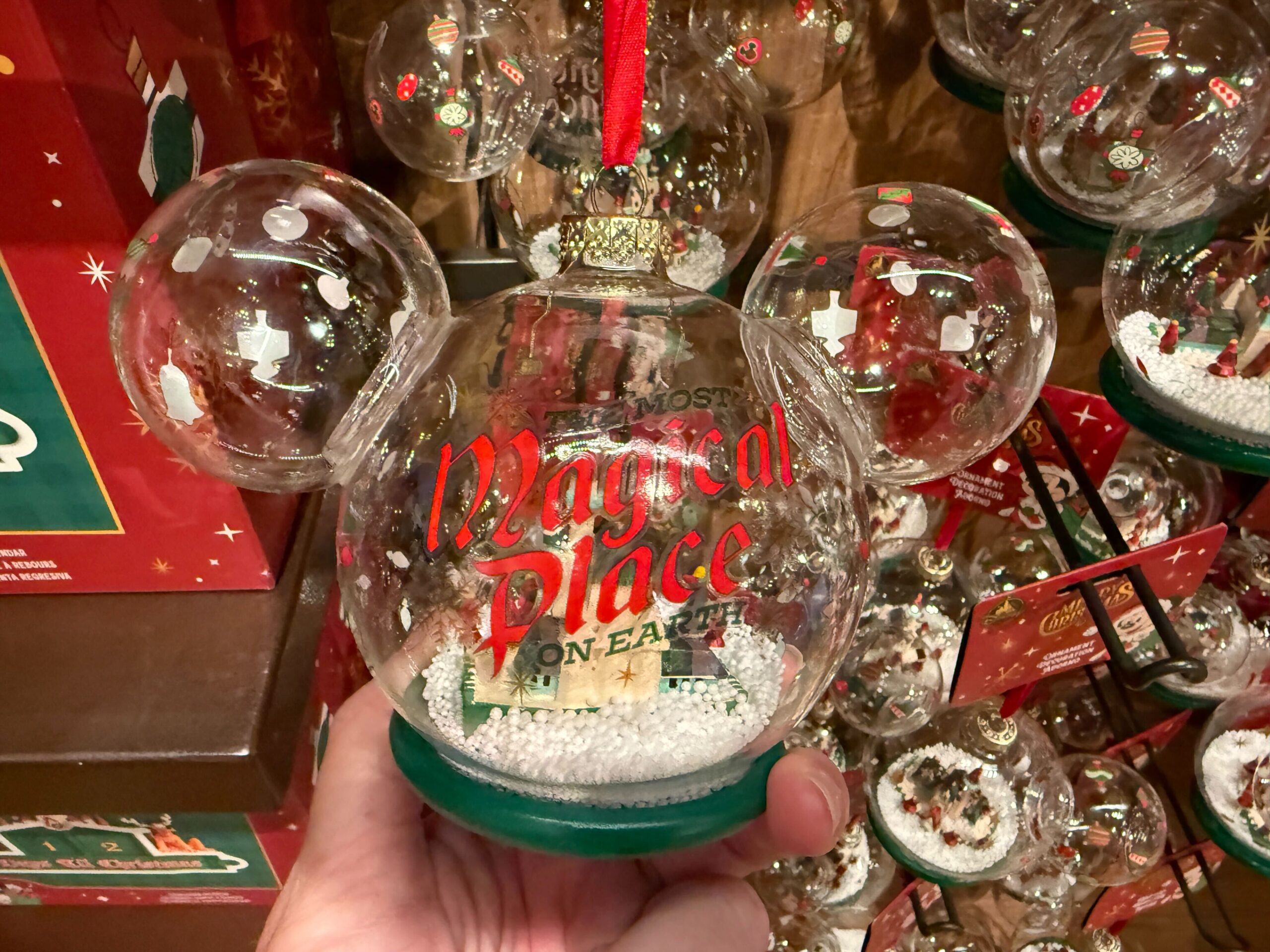 A hand holds a 2025 Disney World Christmas merchandise snow globe with "Most Magical Place on Earth" in red inside.