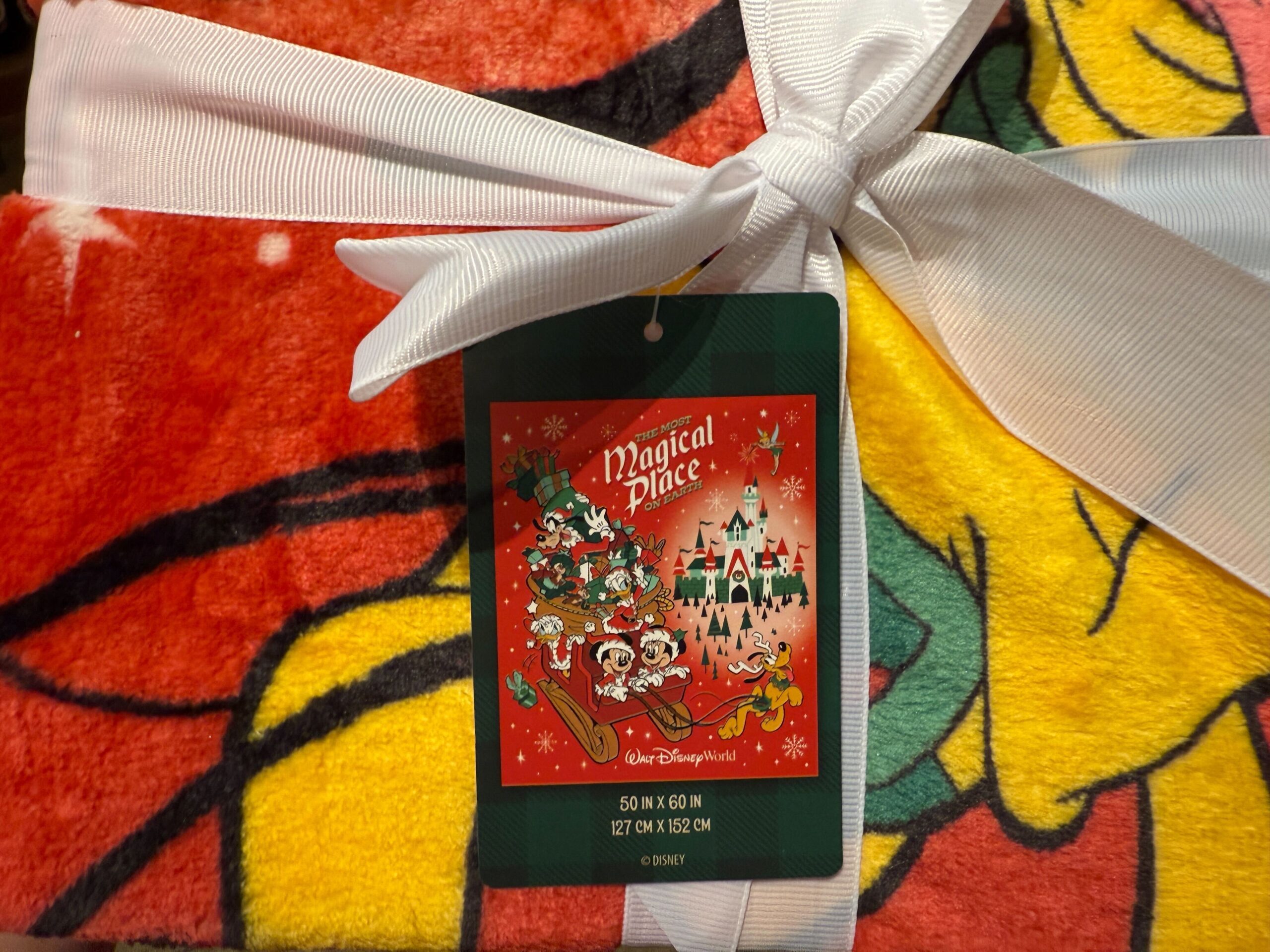 A Walt Disney World Christmas blanket with cartoon characters, wrapped in a white ribbon and festive tag.