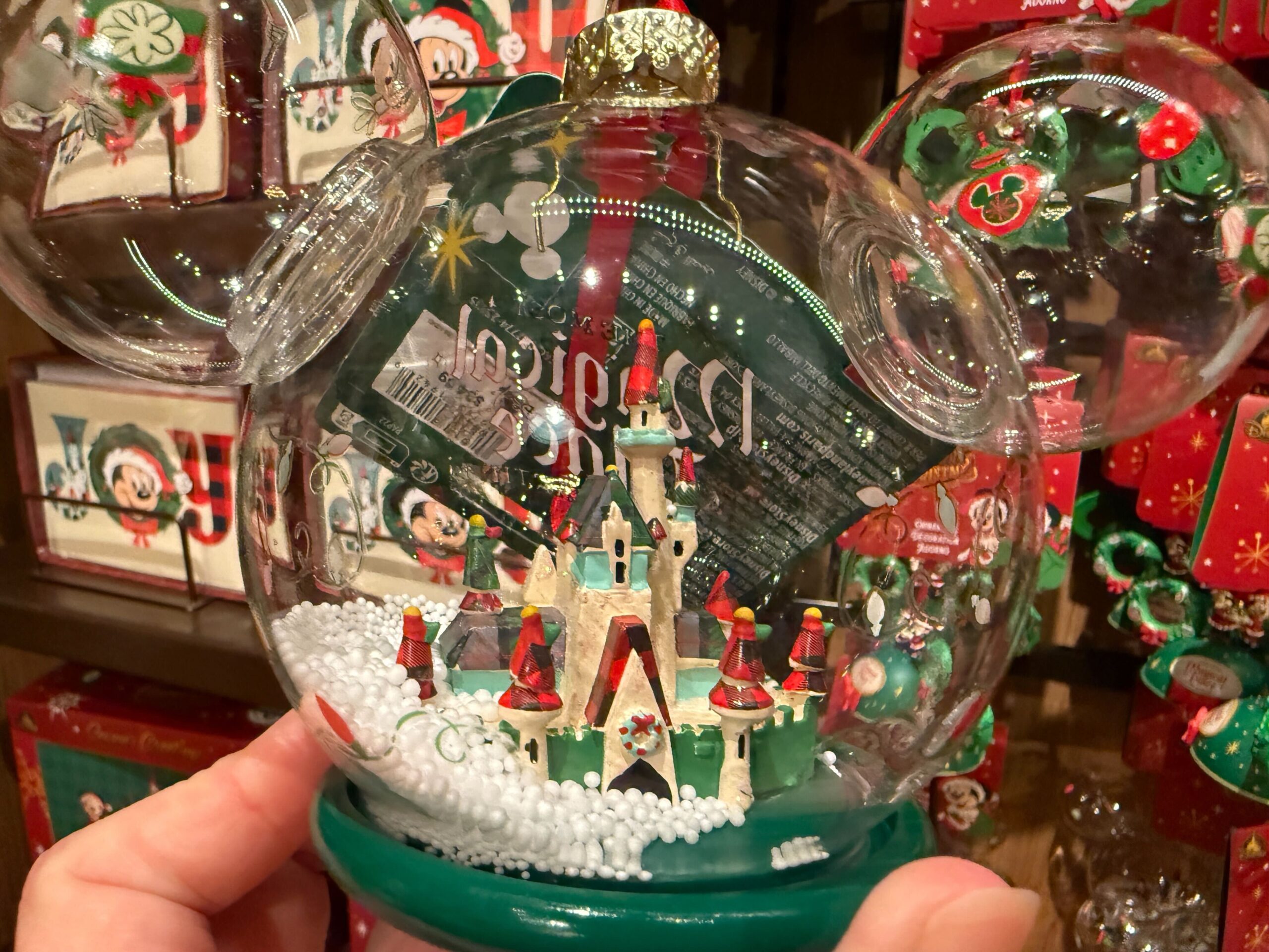 Hand holding 2025 Walt Disney World snow globe with festive castle, Mickey ears, and holiday decorations.