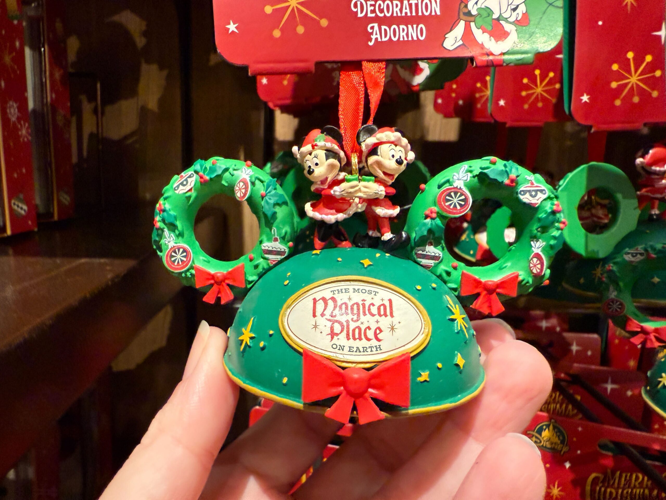 A hand holds a Walt Disney World ornament featuring Minnie and Mickey Mouse in festive holiday outfits with wreaths.