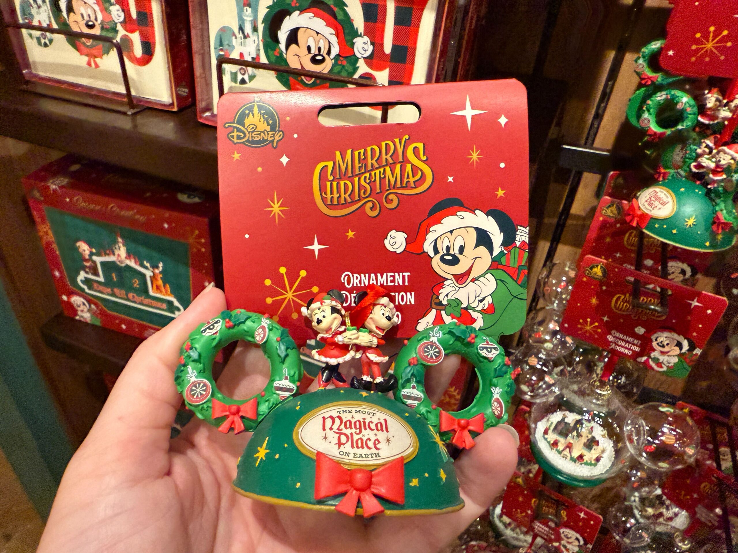 Hand holding a 2025 Disney World Christmas ornament featuring Mickey, Minnie, and festive wreaths—see new merchandise prices.