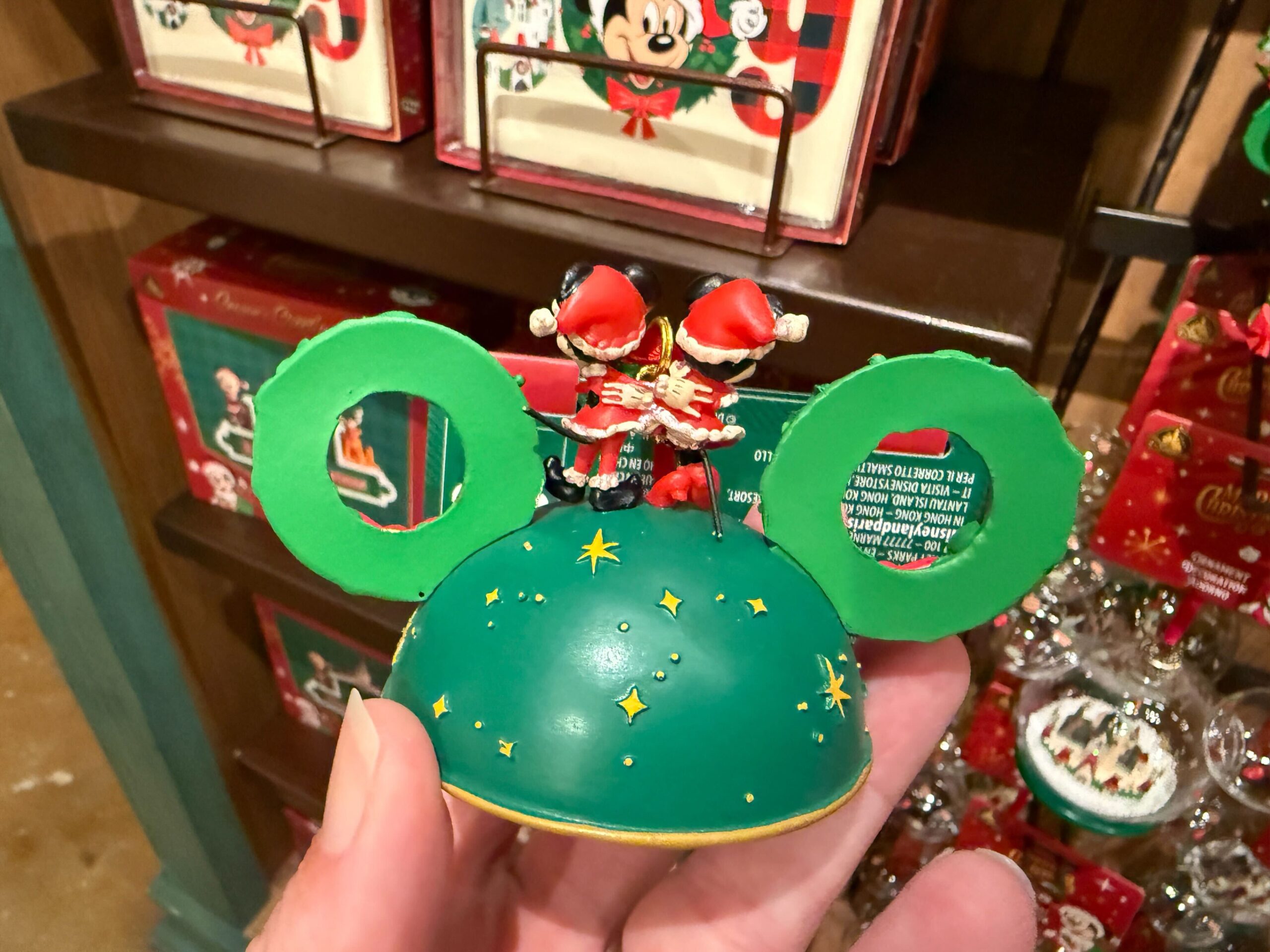 A hand holds a green Mickey Mouse ear ornament, part of the 2025 Walt Disney World Christmas merchandise collection.