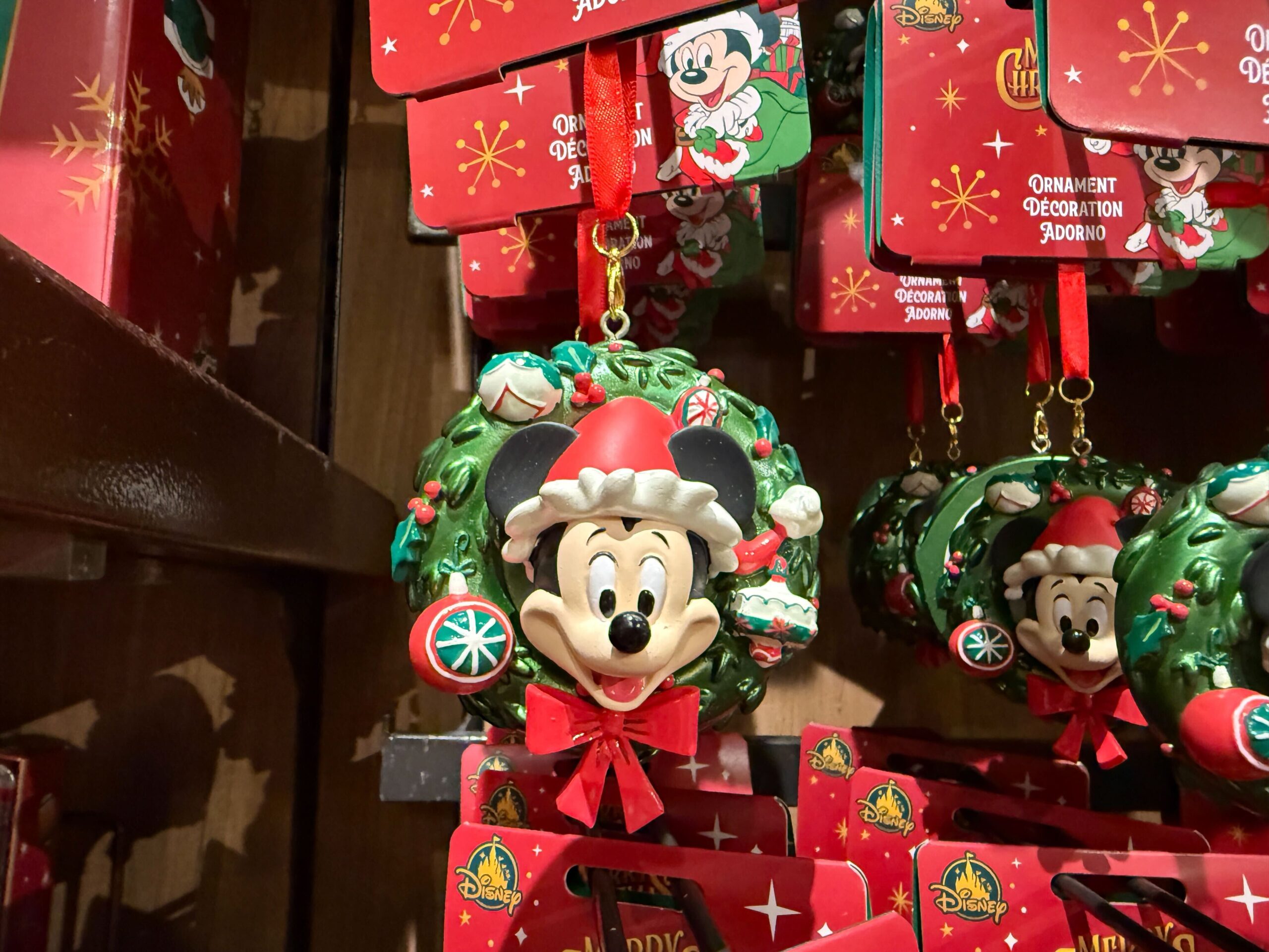 Close-up of a 2025 Mickey Mouse Christmas ornament with a Santa hat, red bow, and festive Walt Disney World decorations in a store.