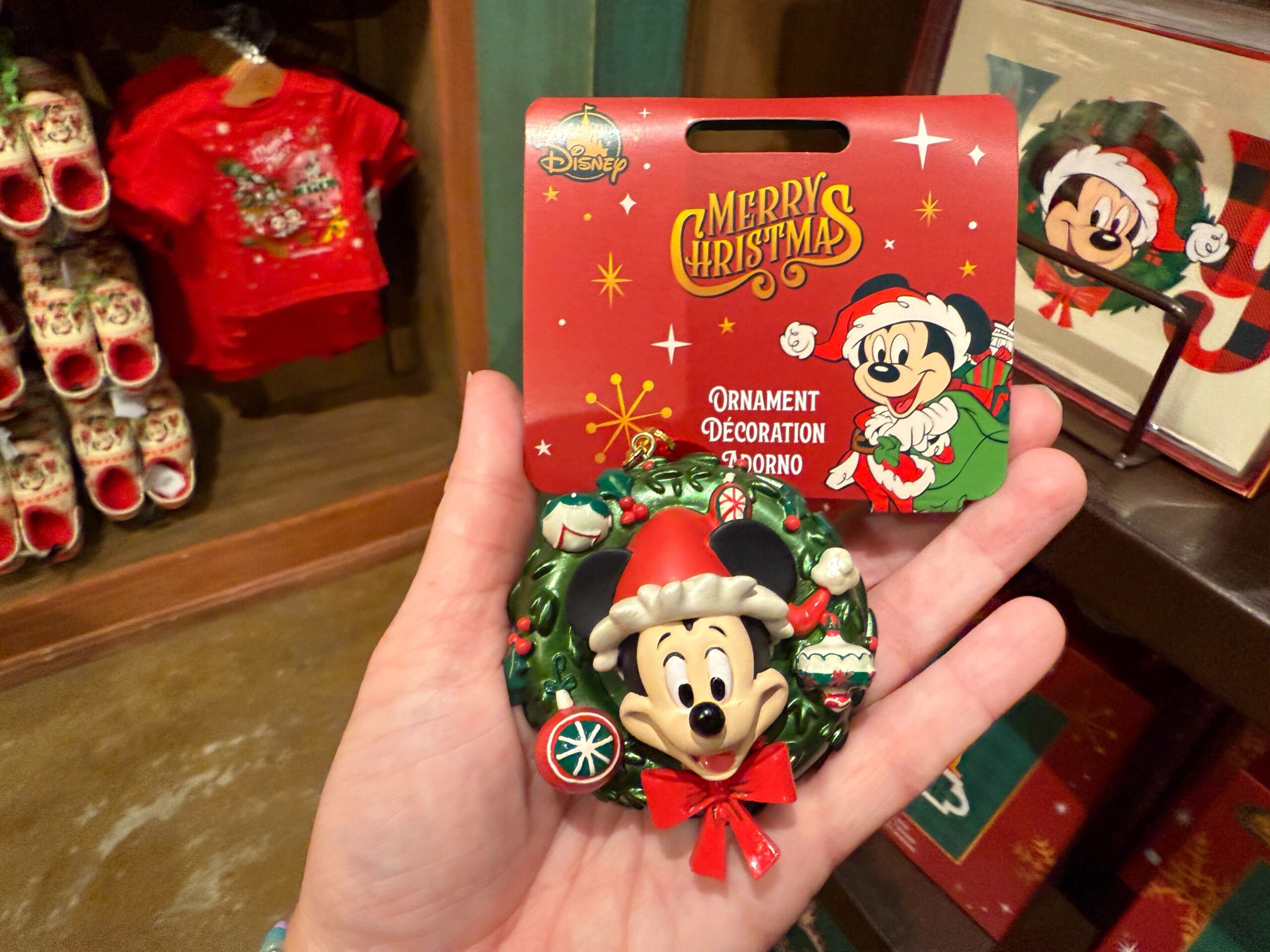 Hand holding a 2025 Walt Disney World Christmas ornament, with festive "Merry Christmas" packaging.