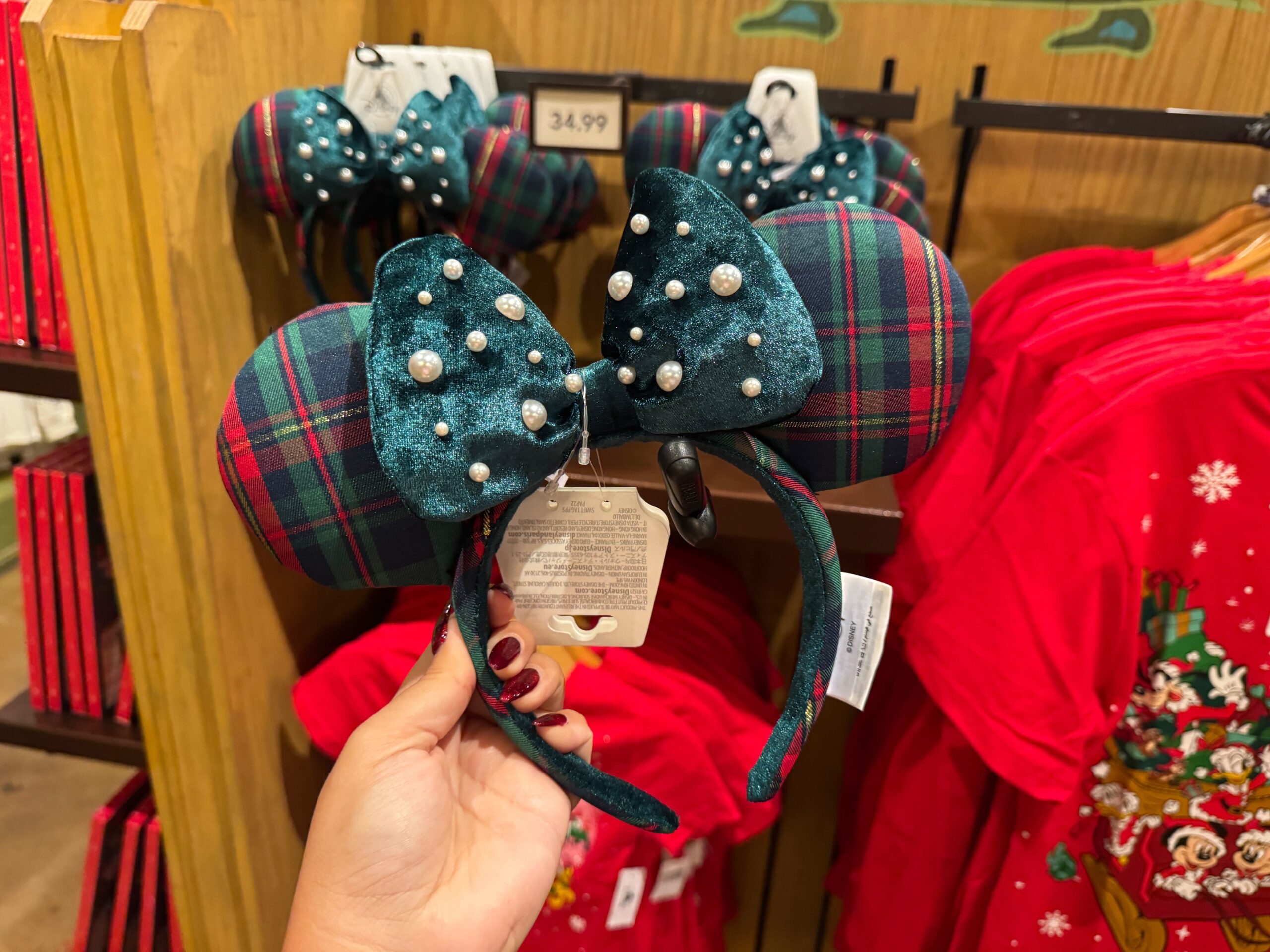 Person holding plaid Minnie Mouse ears with pearl-studded bow among Walt Disney World Christmas merchandise in a store.