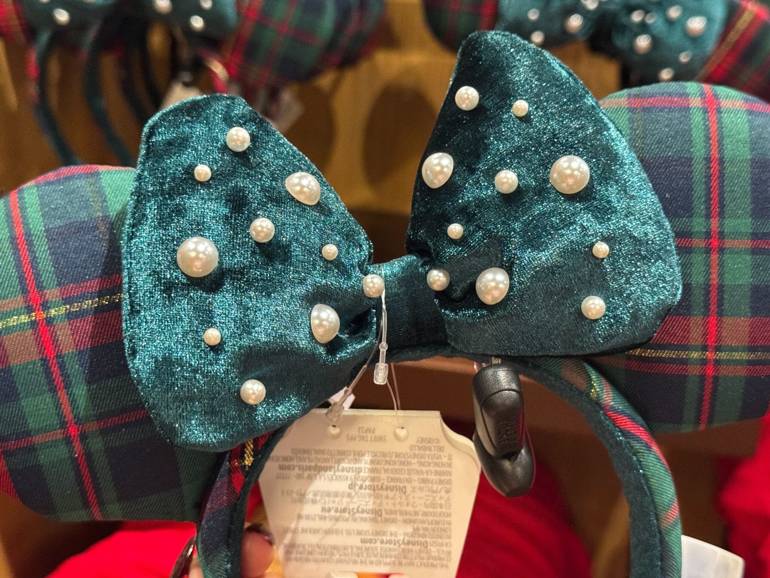 A sparkly teal bow with pearls on a plaid headband, part of 2025 Walt Disney World Christmas merchandise, in a store.
