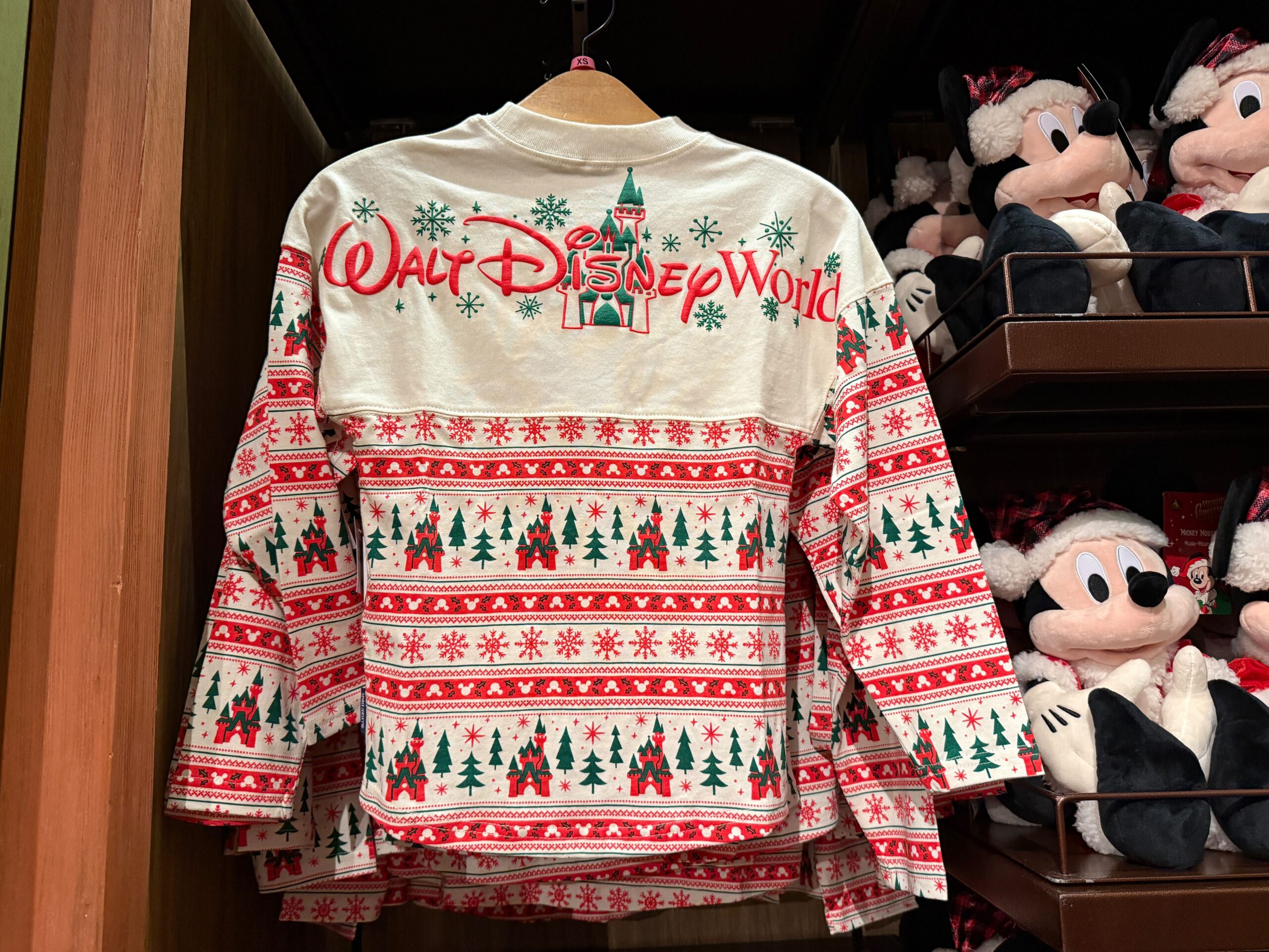 A 2025 Walt Disney World shirt with festive red, green, and white patterns hangs near Mickey Christmas merchandise.