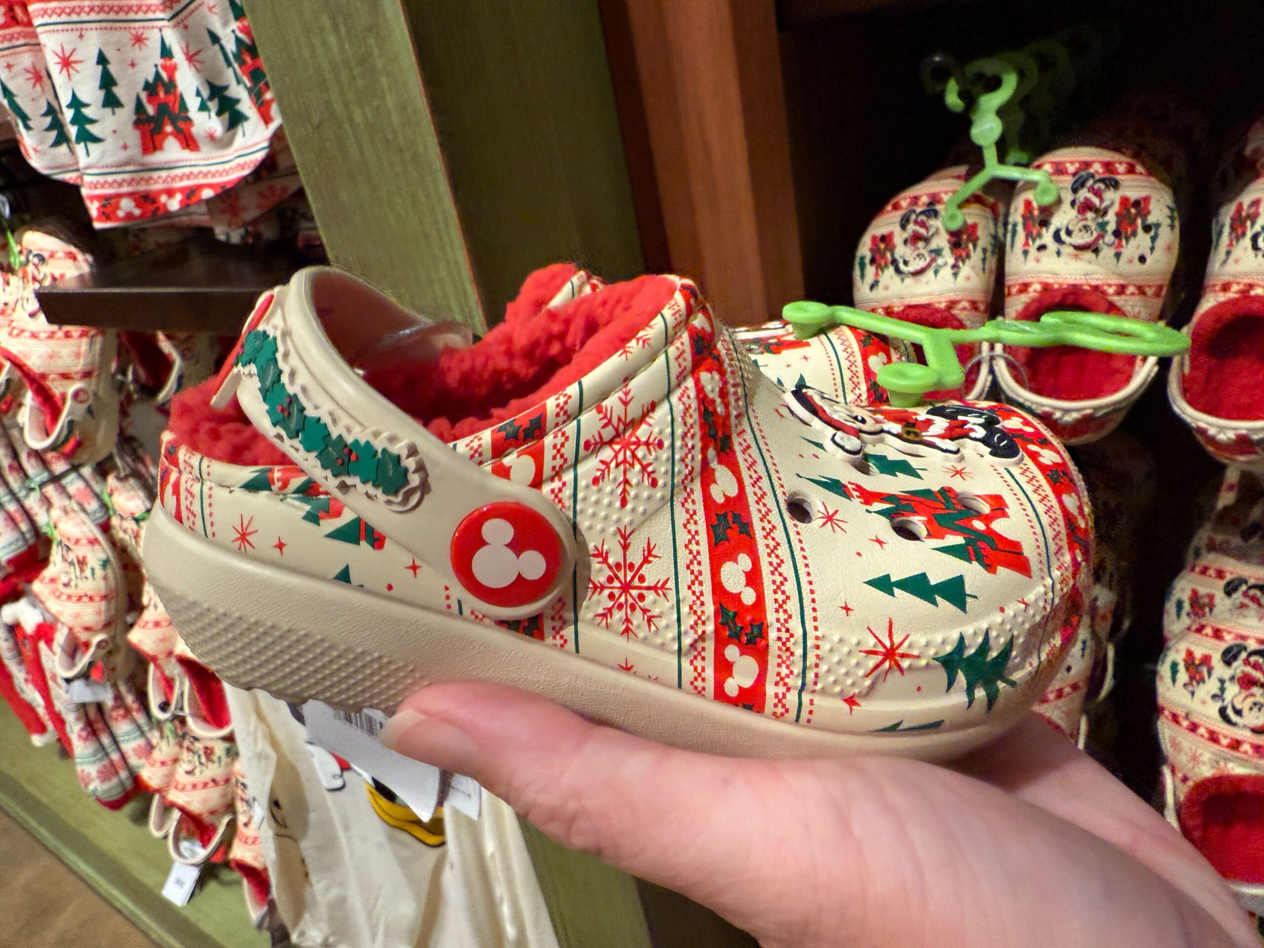 A hand holds a festive holiday clog with Walt Disney World patterns and red fleece, displayed as Christmas merchandise.