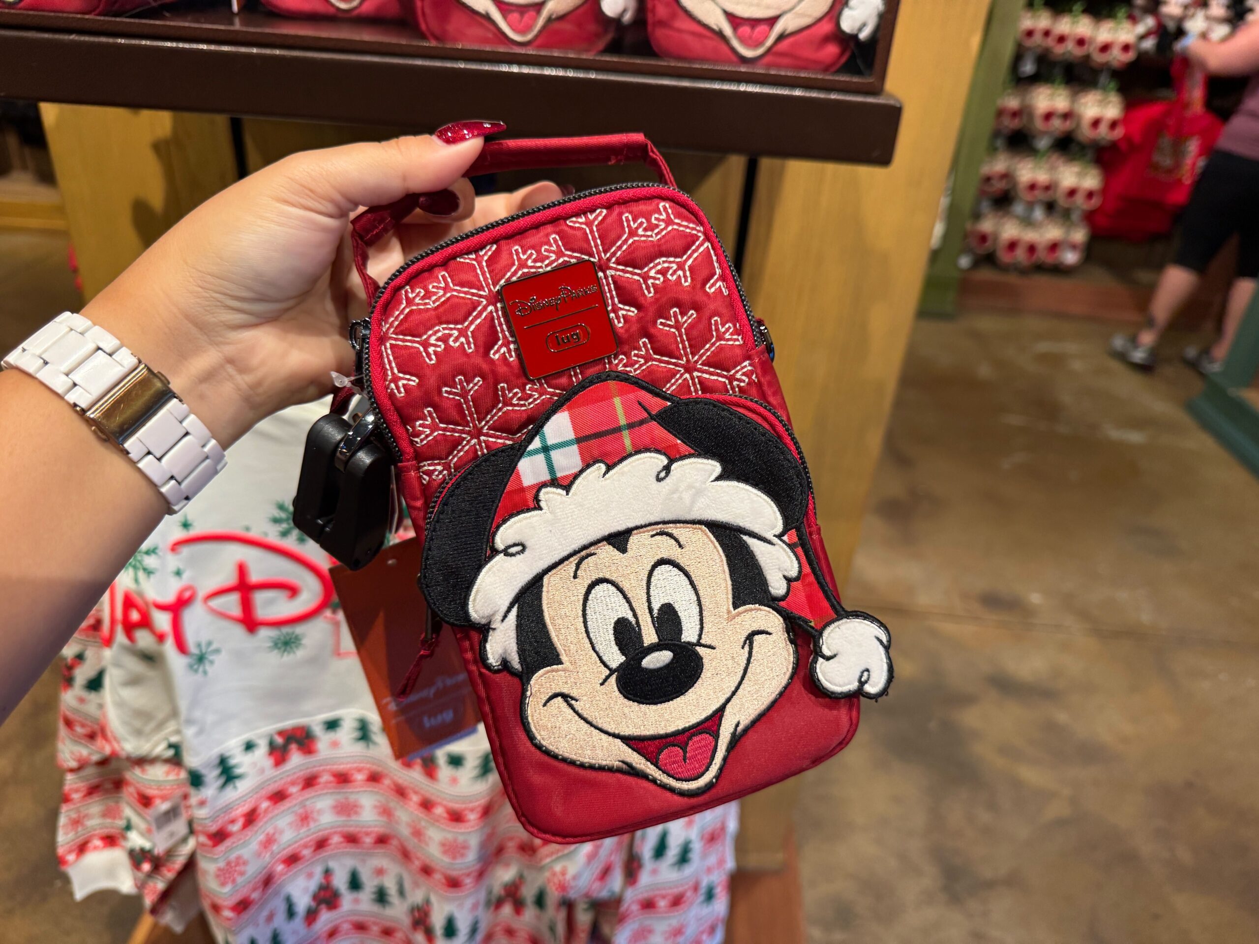 A hand holds Walt Disney World Christmas merchandise: a red bag with Mickey Mouse in a Santa hat and festive decorations.