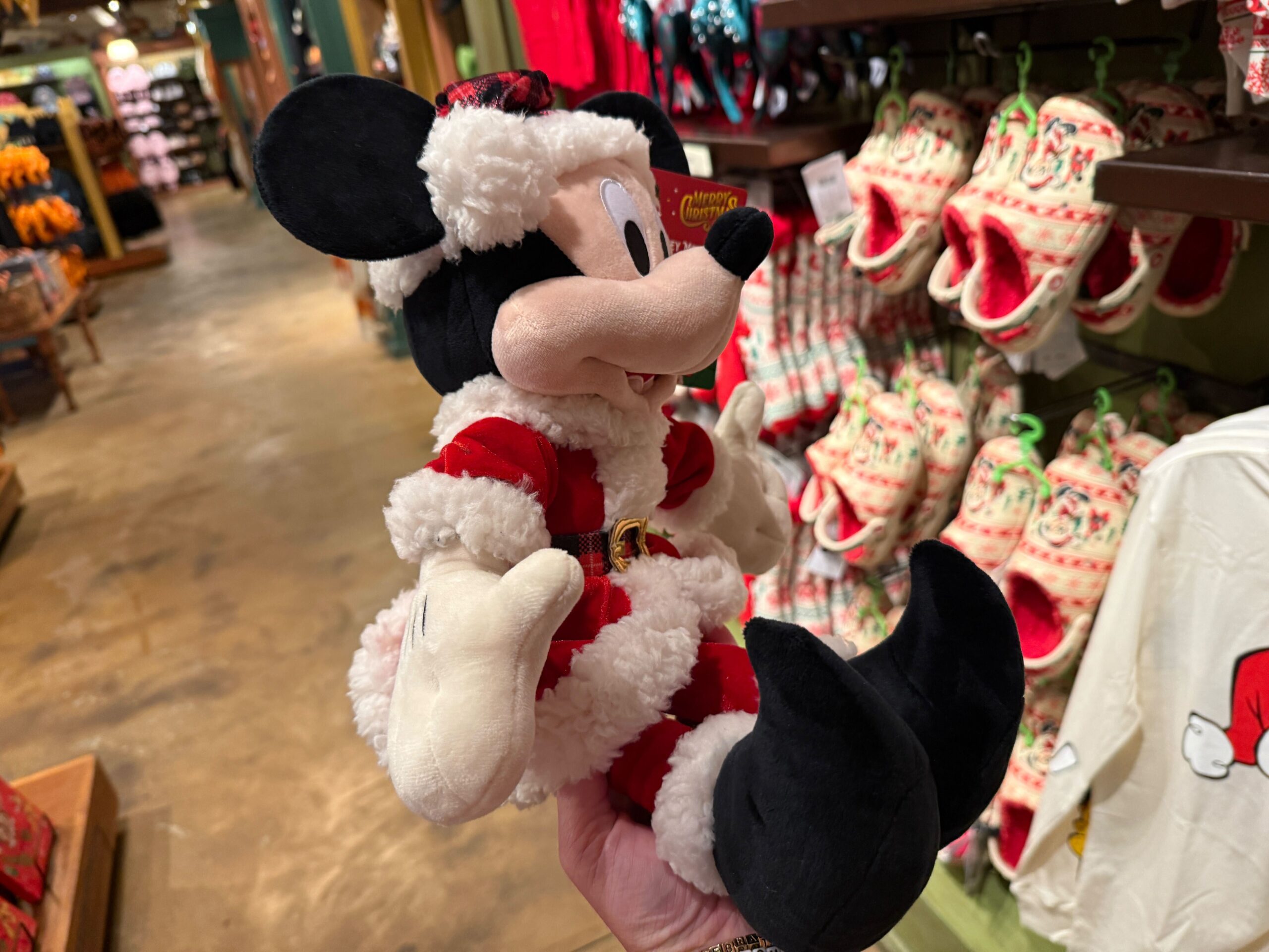 A hand holds a Minnie Mouse Santa plush, part of 2025 Disney merchandise in a store with holiday-themed items.