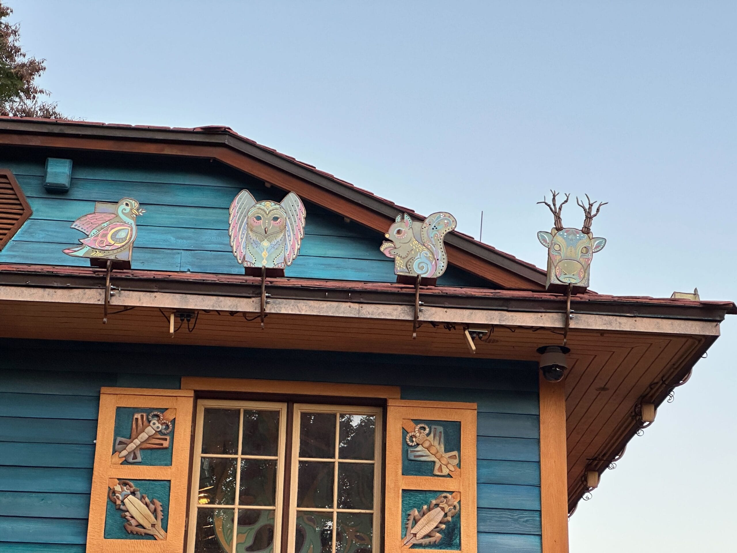 Four whimsical animal cutouts, like Disney park holiday decor, are displayed above a blue building beneath a bright, clear sky.