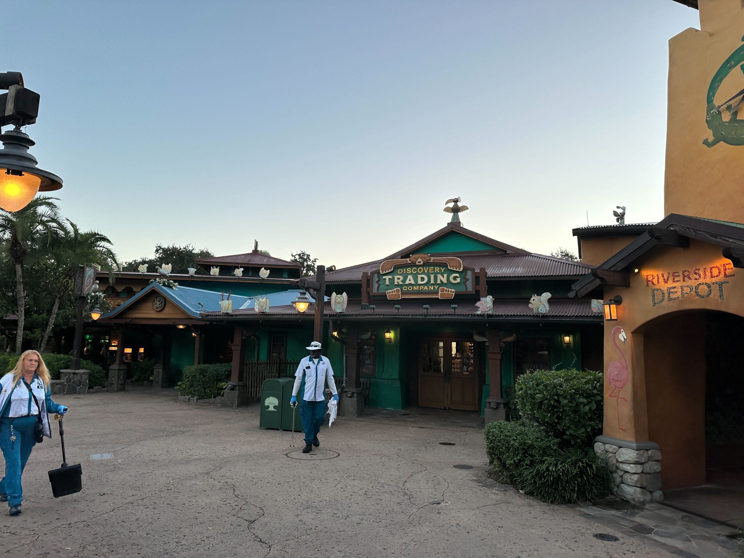 Two guests stroll by festive Christmas decor outside Discovery Trading Company at Disney's Animal Kingdom during dusk—no castle in view.