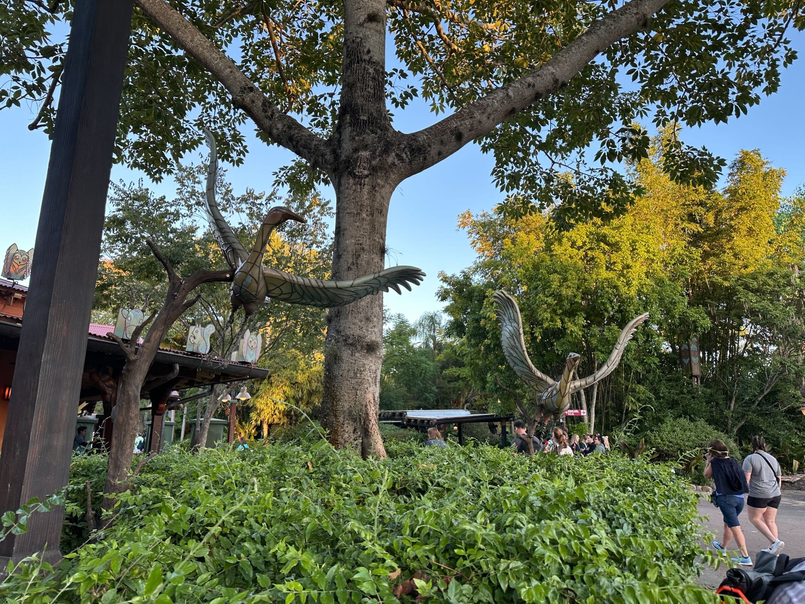 Metal bird ornaments hang in a tree with lush greenery below, bringing holiday cheer to Disney's Animal Kingdom, no castle in view.
