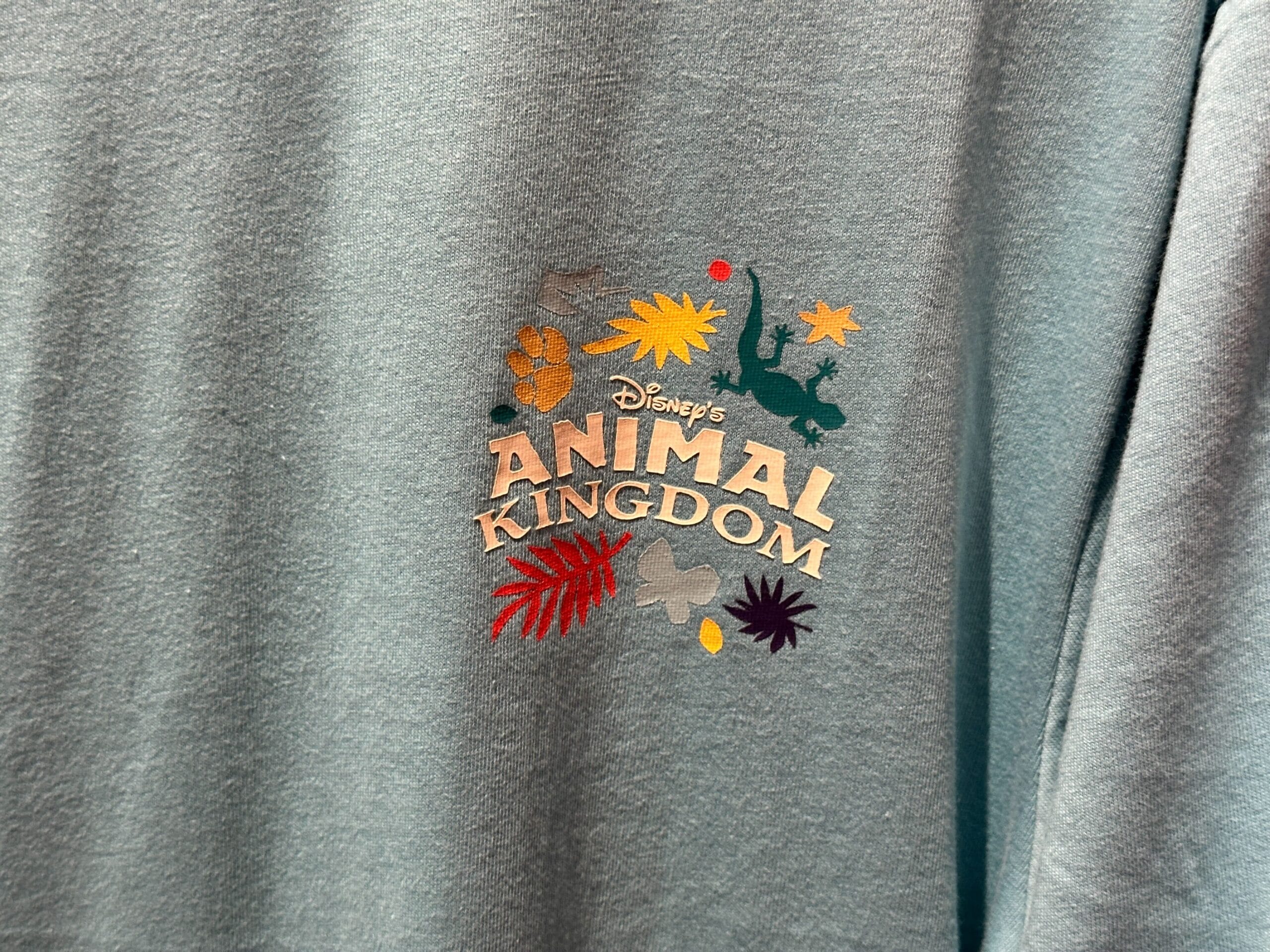Blue shirt with Disney’s Animal Kingdom logo and animal tracks, Circle of Life merch—not featuring any castle from Disney parks.