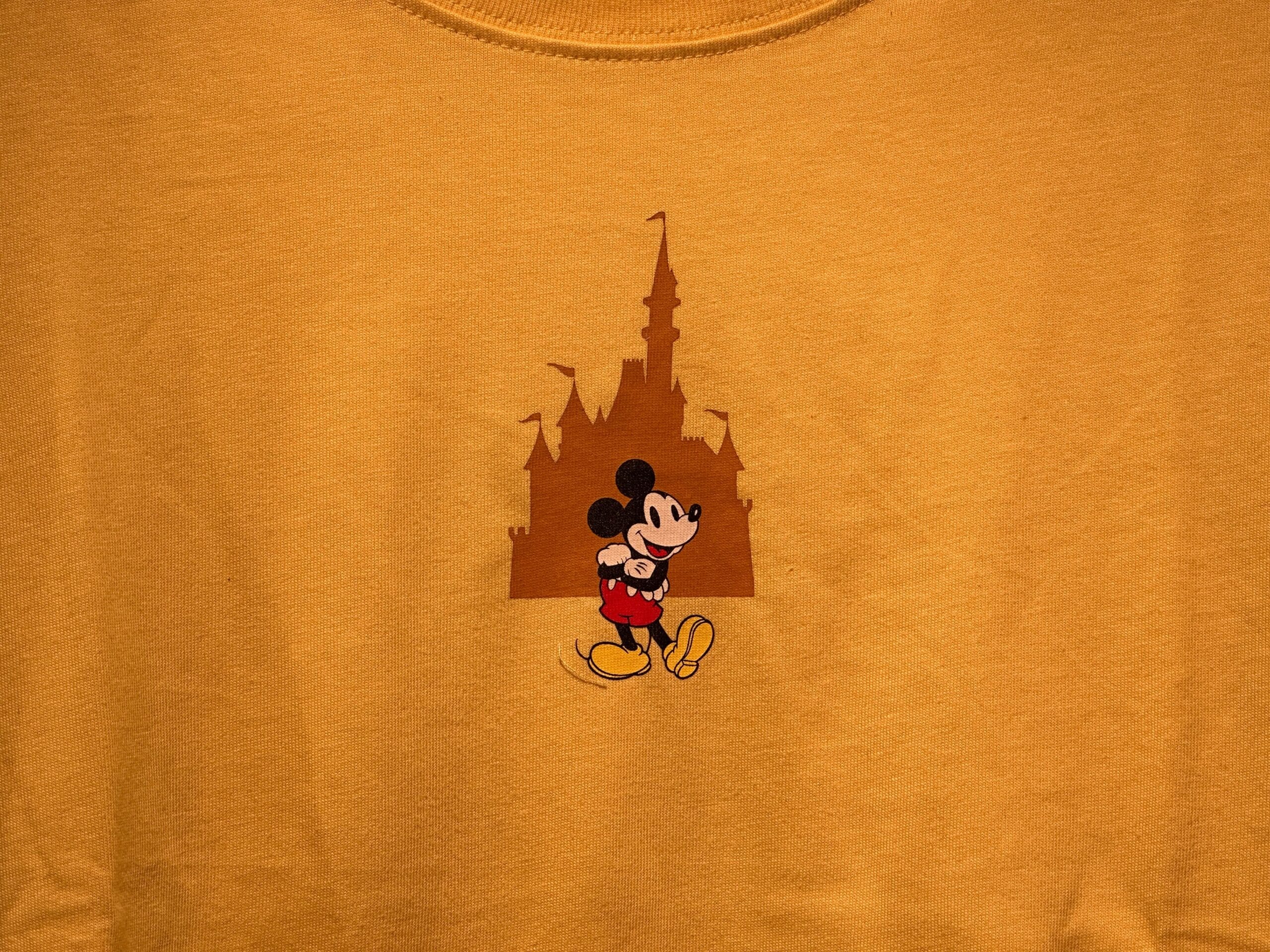 Yellow shirt with Mickey Mouse walking before a castle silhouette resembling Cinderella Castle from Walt Disney World, centered.