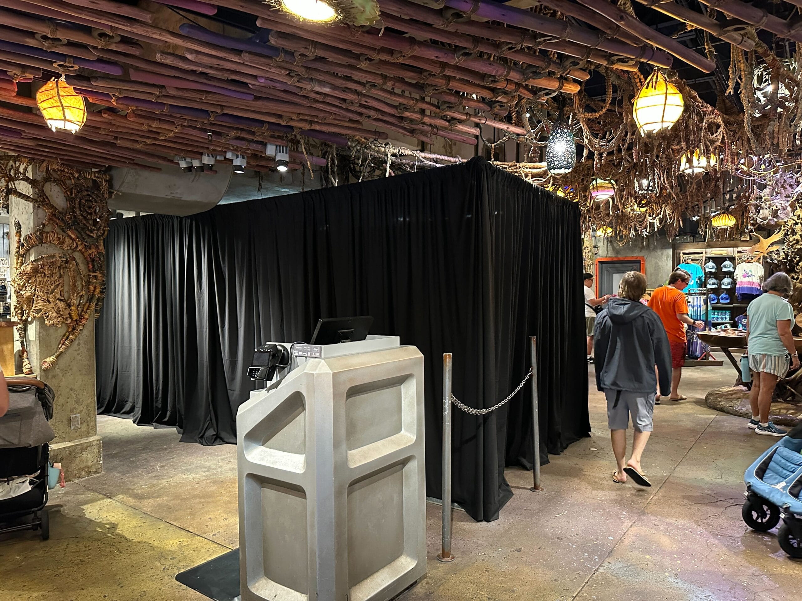 A black curtain booth in the World of Avatar store, with people shopping beneath Pandora-inspired decorative lights.