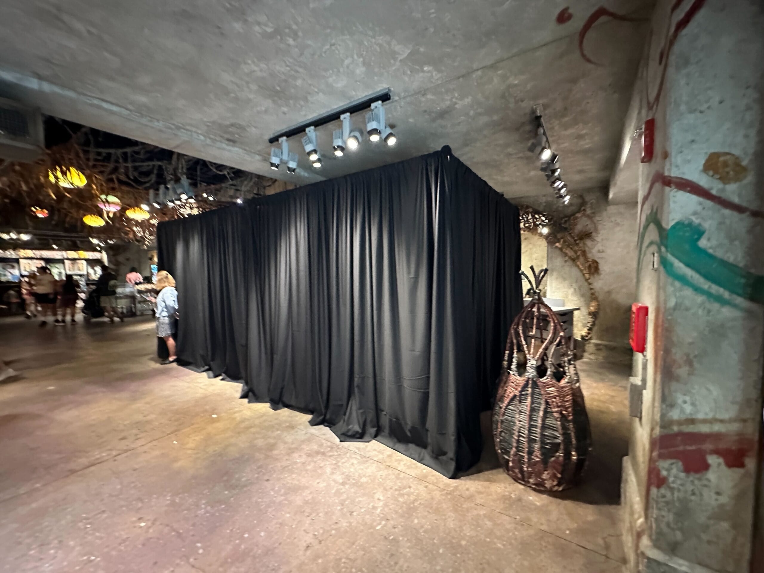 A black curtain enclosure stands in Pandora - The World of Avatar, with people and themed decor nearby.