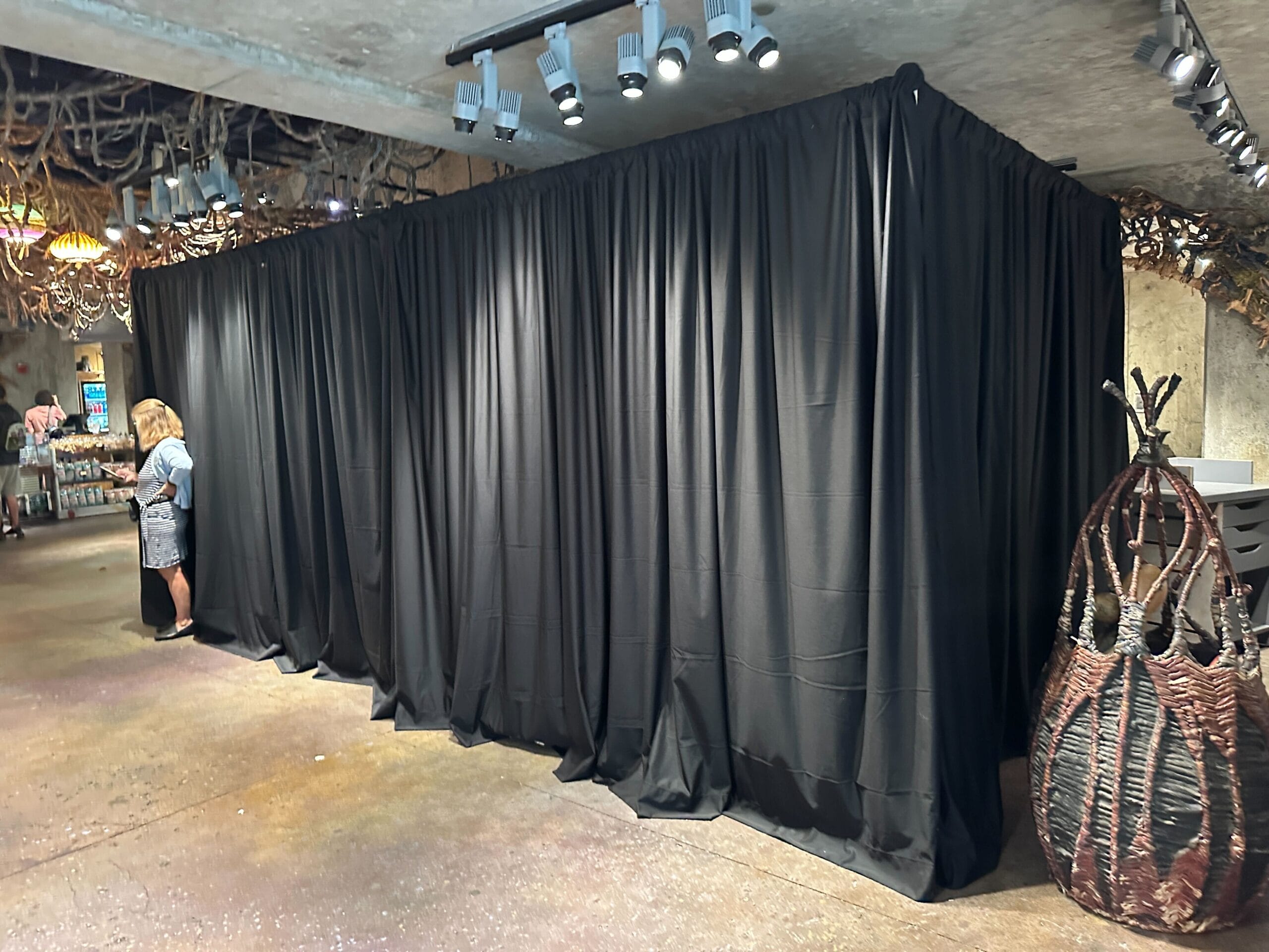 A large black curtain enclosure offers a unique experience in a store, with a woman using her phone nearby.