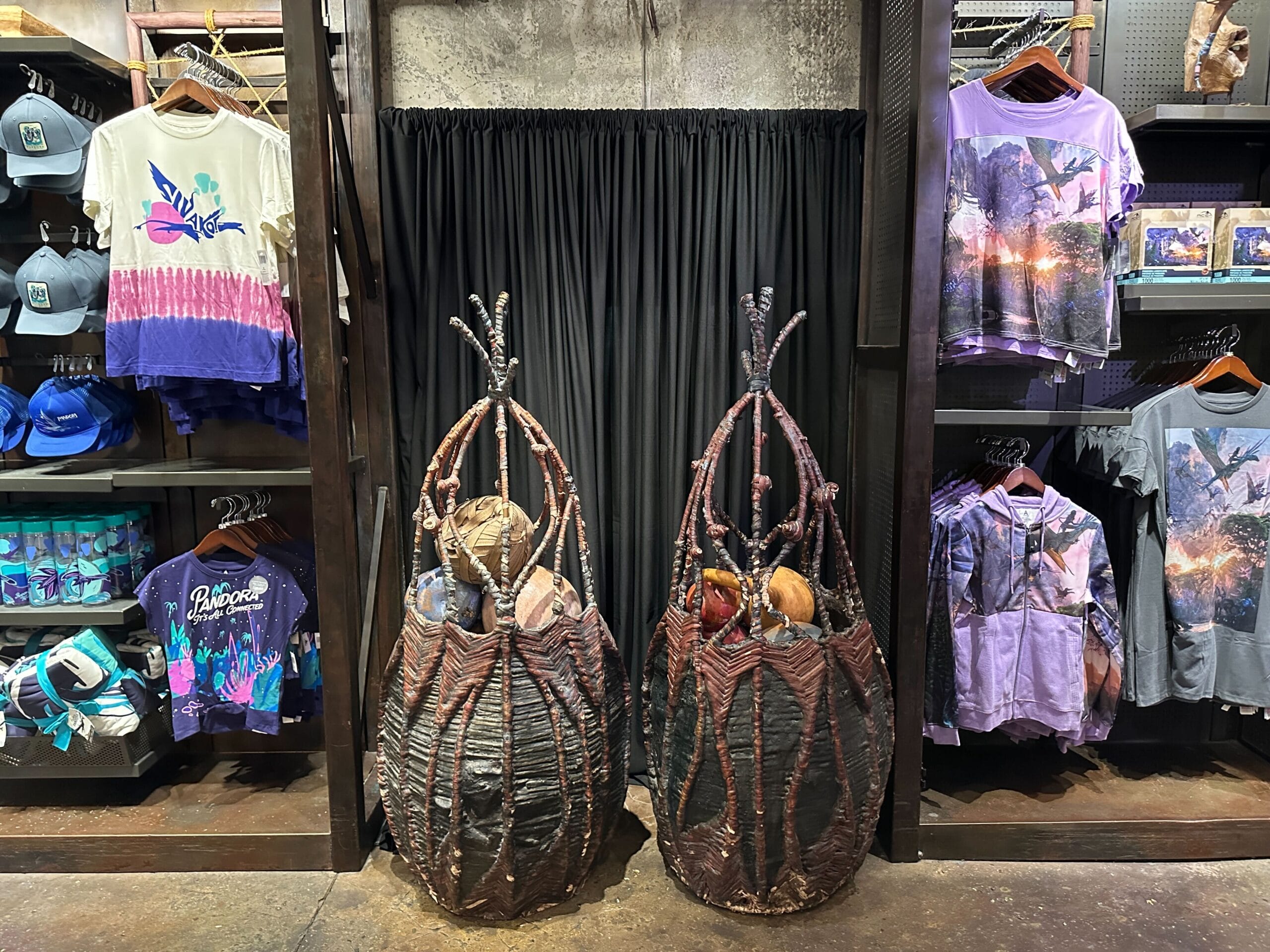 Two decorative baskets with faux alien eggs in front of colorful Pandora - The World of Avatar shirts and hats.