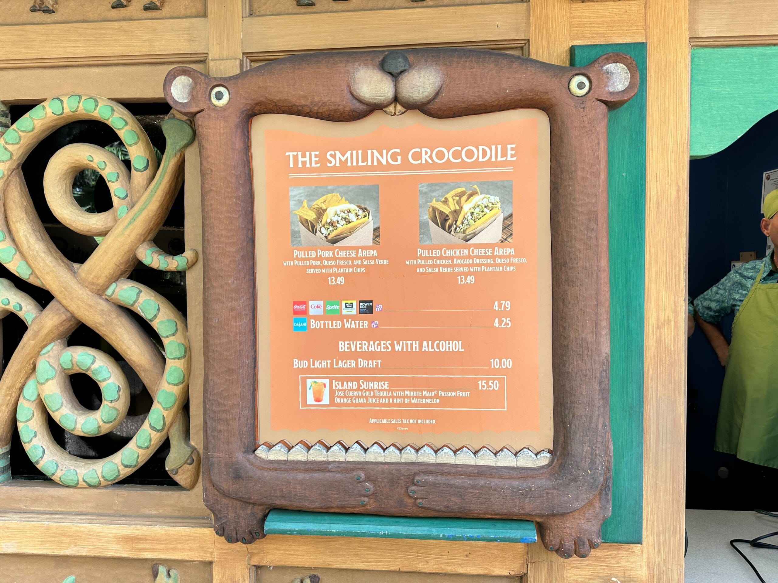The Smiling Crocodile menu board at a Disney park with pulled pork, chicken cheese arots, POG Limeade, and drinks.