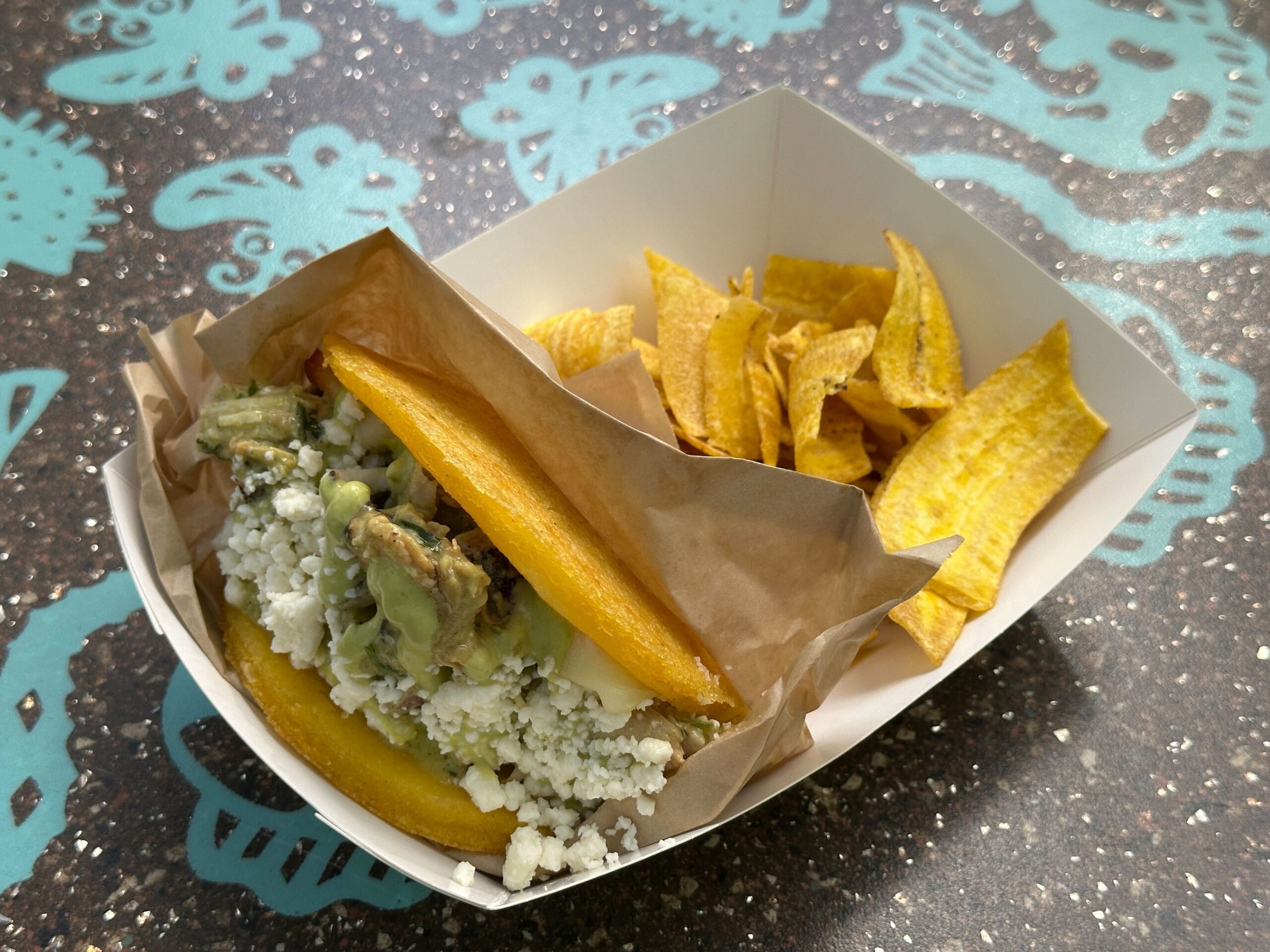At Terra Treats in Disney's Animal Kingdom, a tray with an arepa, cheese, avocado, and plantain chips sits on a vibrant table.
