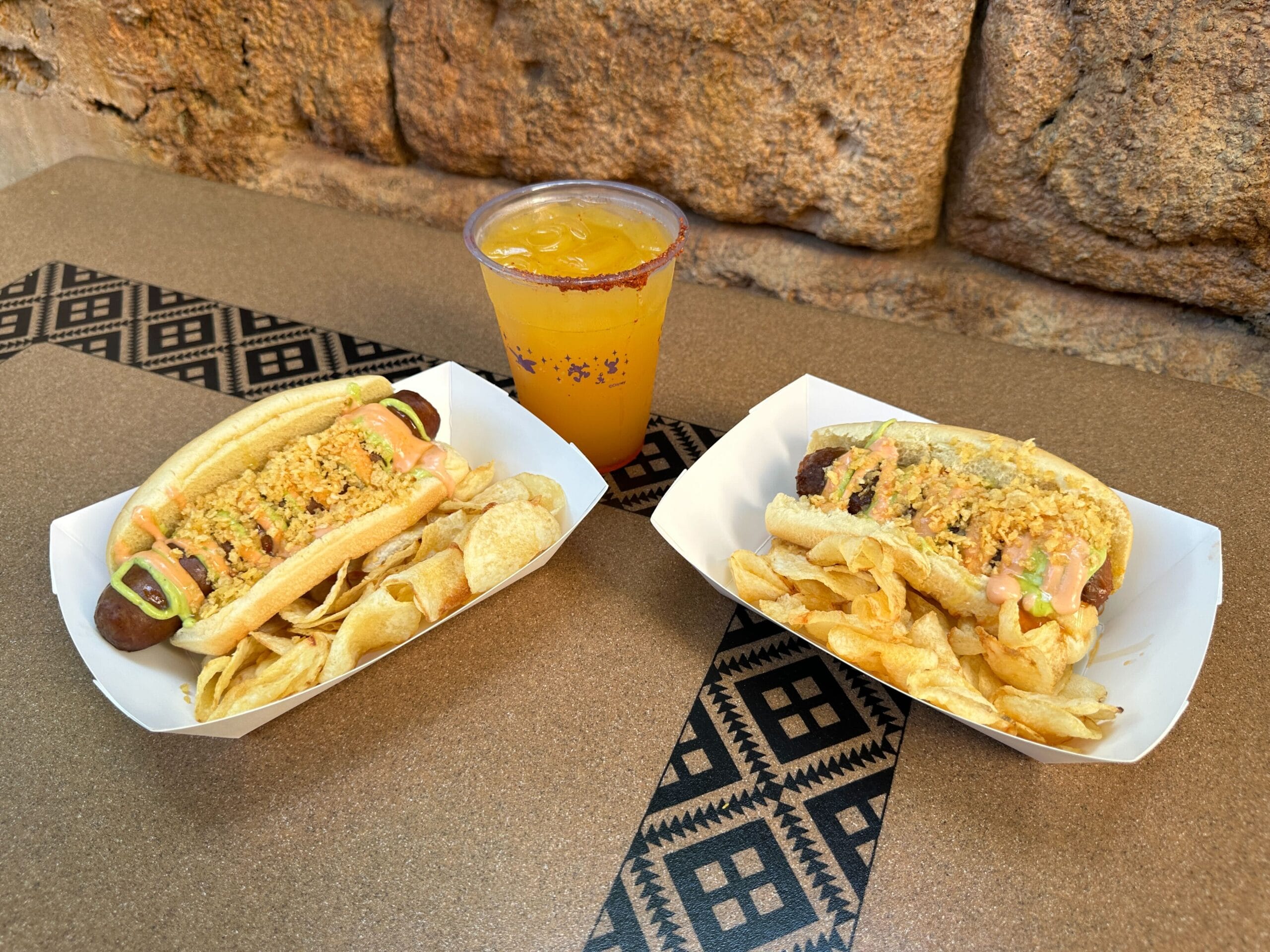 Colombian-Style Hot Dogs with chips and POG Limeade at Terra Treats in Disney’s Animal Kingdom, set on a brown patterned table.
