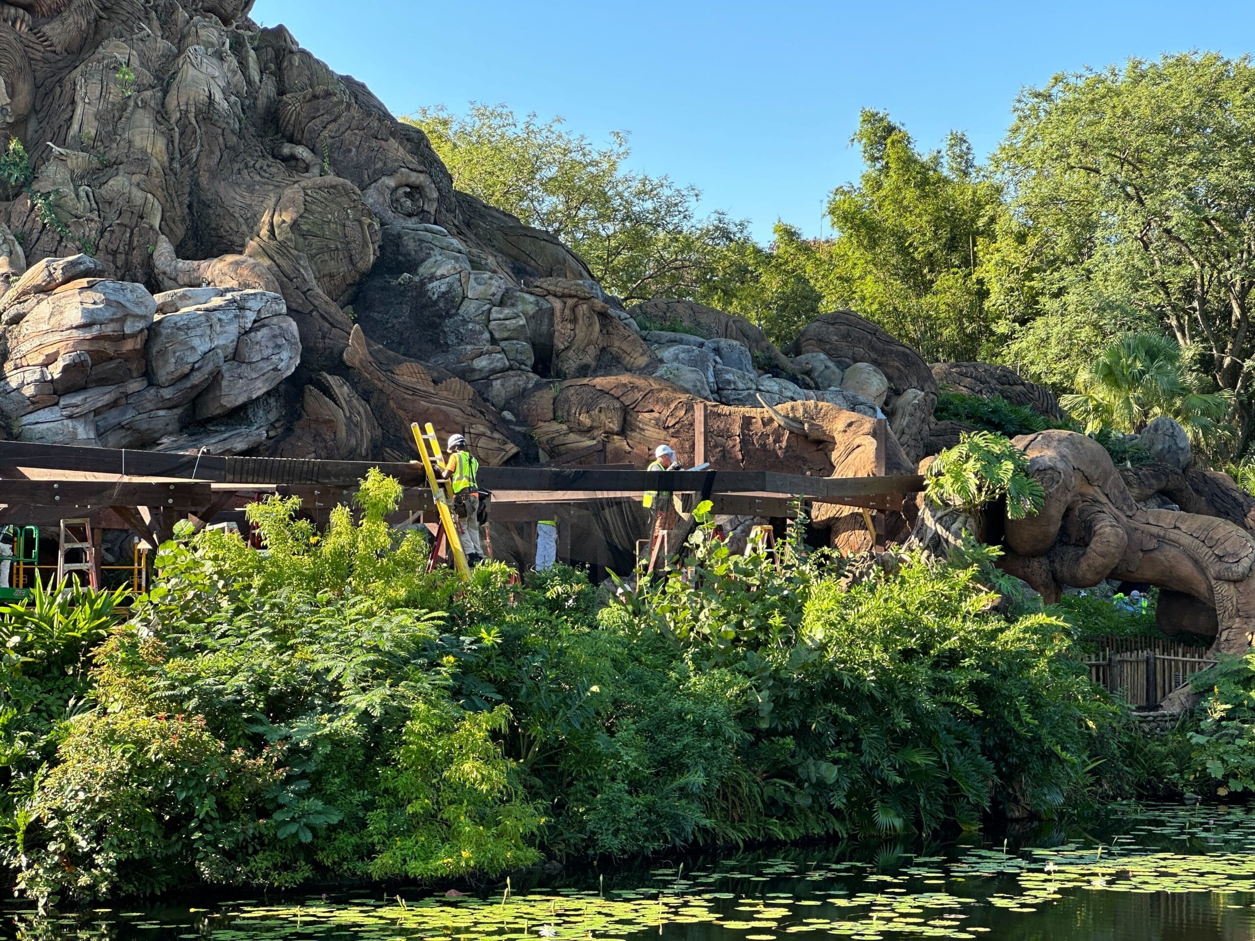 Rocky hillside with Zootopia animal carvings, lush plants, lily pad pond, and show sign—evoking Disney park detail and charm.