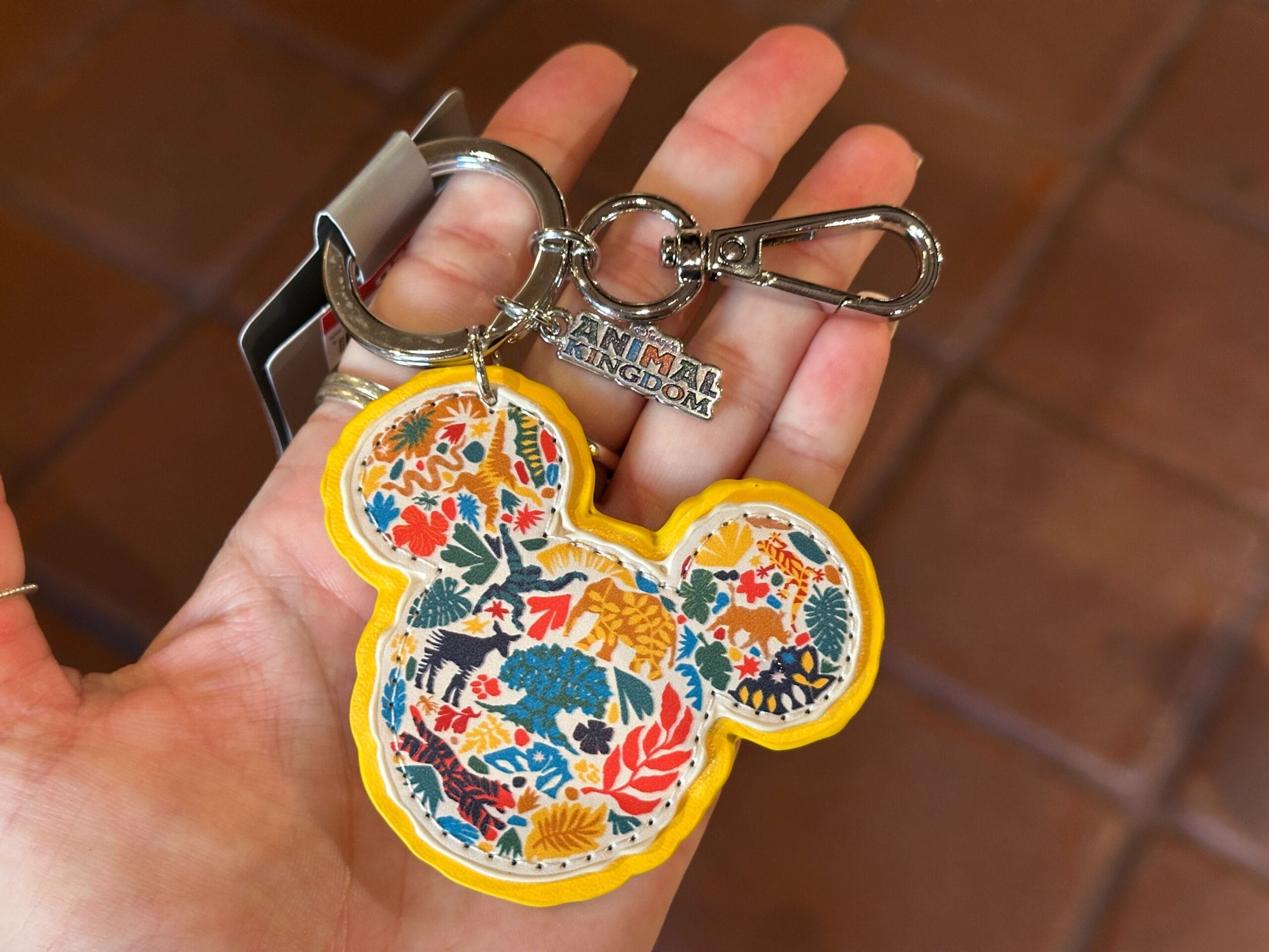 A hand displays a Mickey Mouse-shaped keychain from Disney's Animal Kingdom, decorated with vibrant animal motifs—no castle pictured.