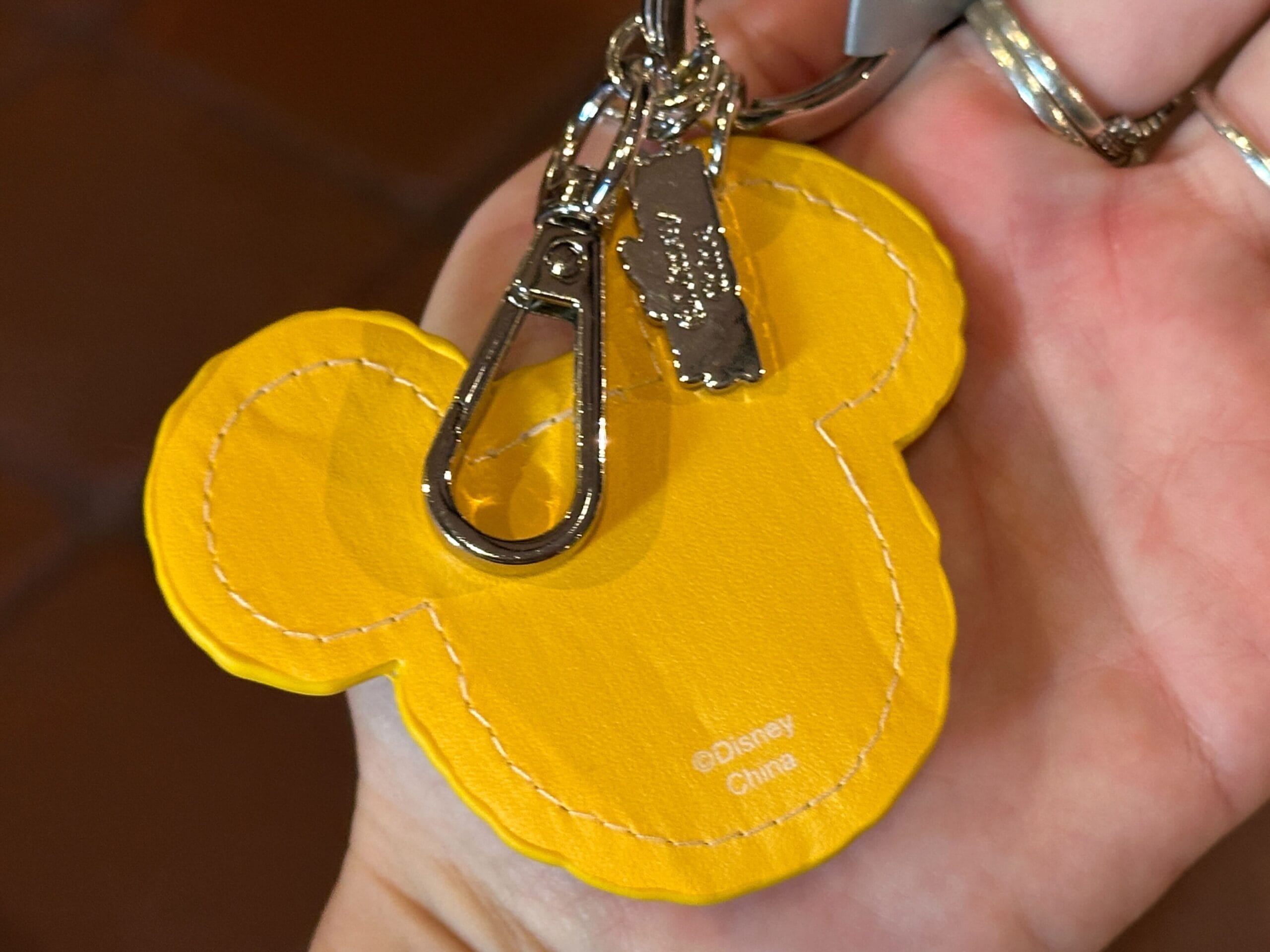 A hand holds a yellow Mickey Mouse-shaped keychain with metal hardware and a "Disney Animal Kingdom" label, unique to Walt Disney World.