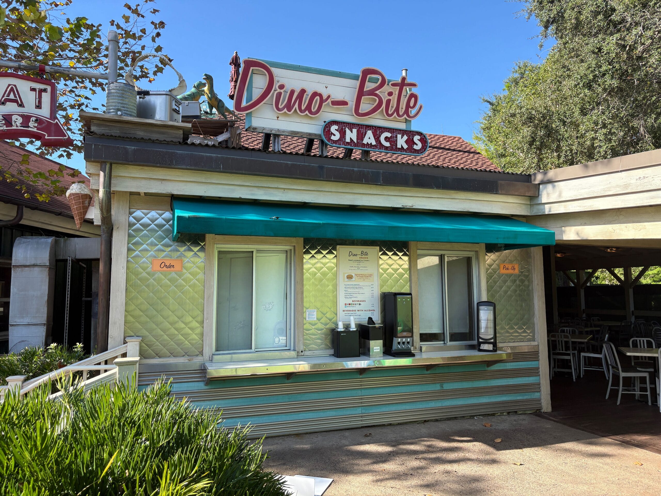 Dino-Bite Snacks food stand with a teal awning and outdoor seating, located near Trilo-Bites in Disney's Animal Kingdom. No castle shown.
