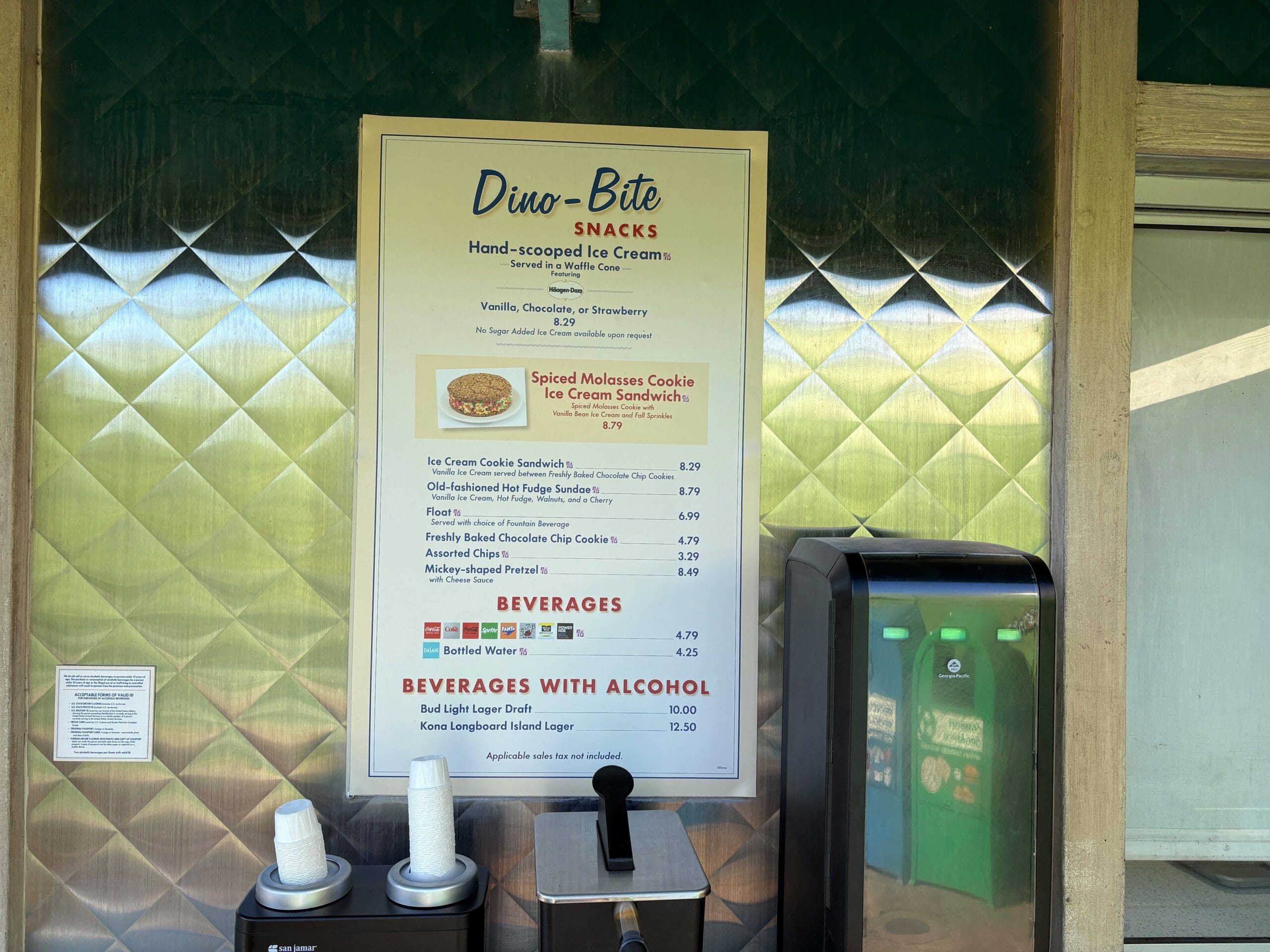 Menu board at Dino-Bite Snacks in Disney’s Animal Kingdom lists ice cream treats and beverages, with drink dispensers below—no castle pictured.