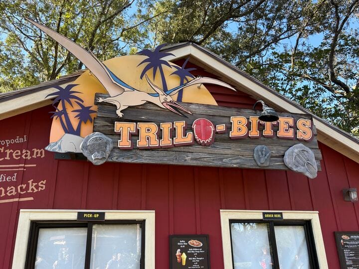 A "TRILO-BITES" sign with a pterosaur and fossils above a red snack stand at Disney's Animal Kingdom, no castle in sight.