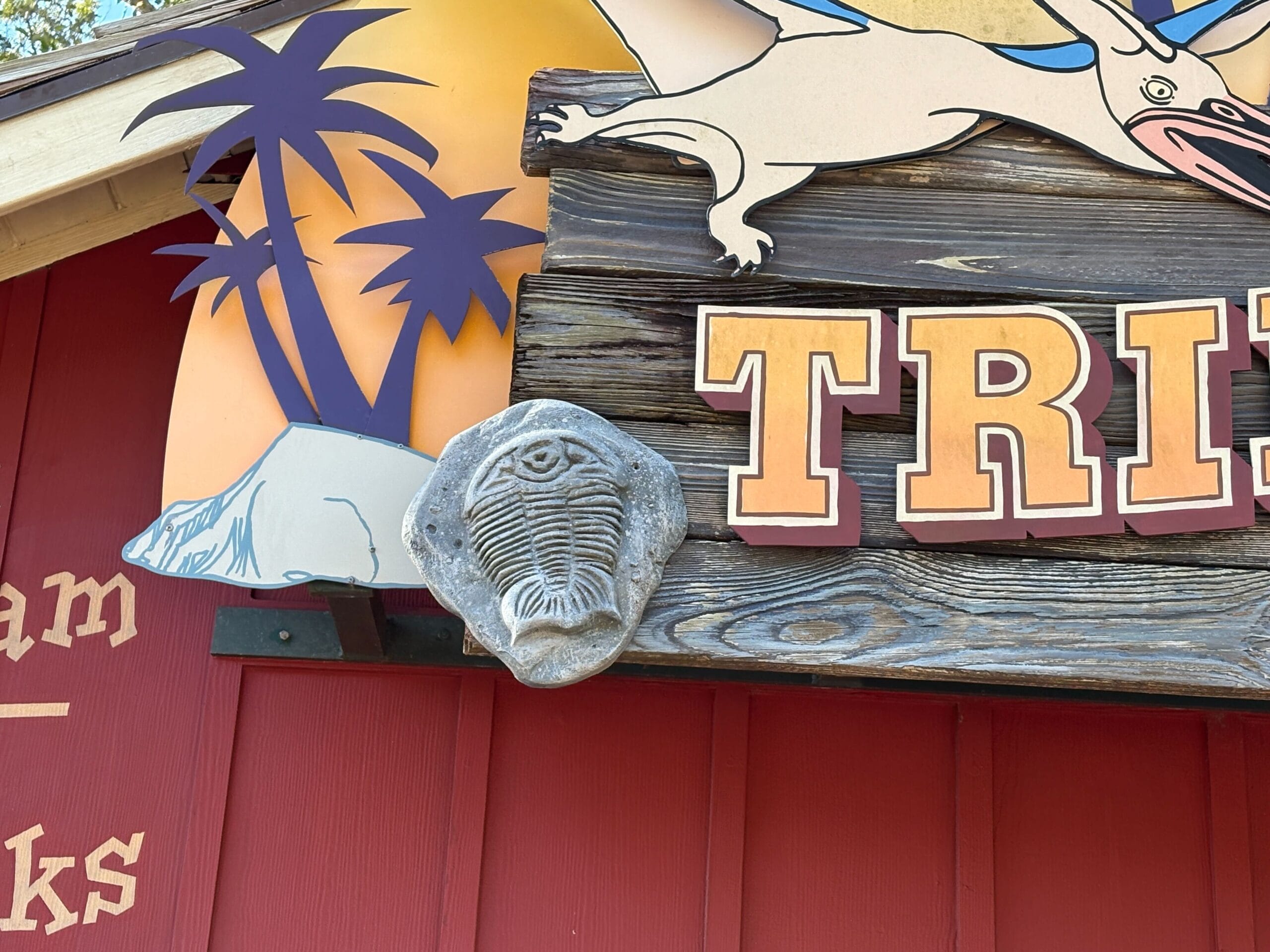 A gray trilobite fossil sits atop the Trilo-Bites sign in Disney's Animal Kingdom, surrounded by dino accents—no castle nearby.