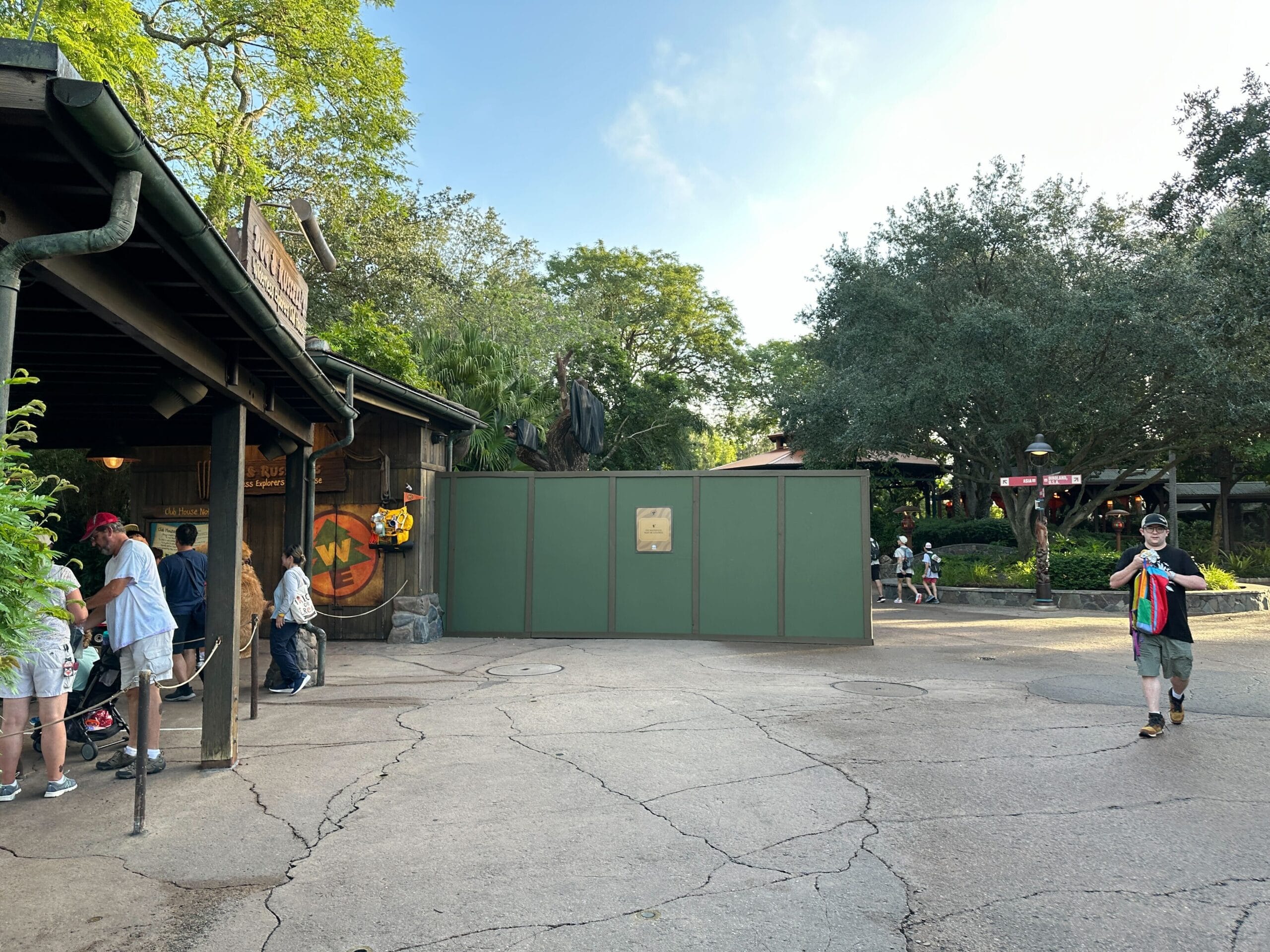 Green construction walls block part of an Animal Kingdom pathway near a building; a few people are walking nearby.