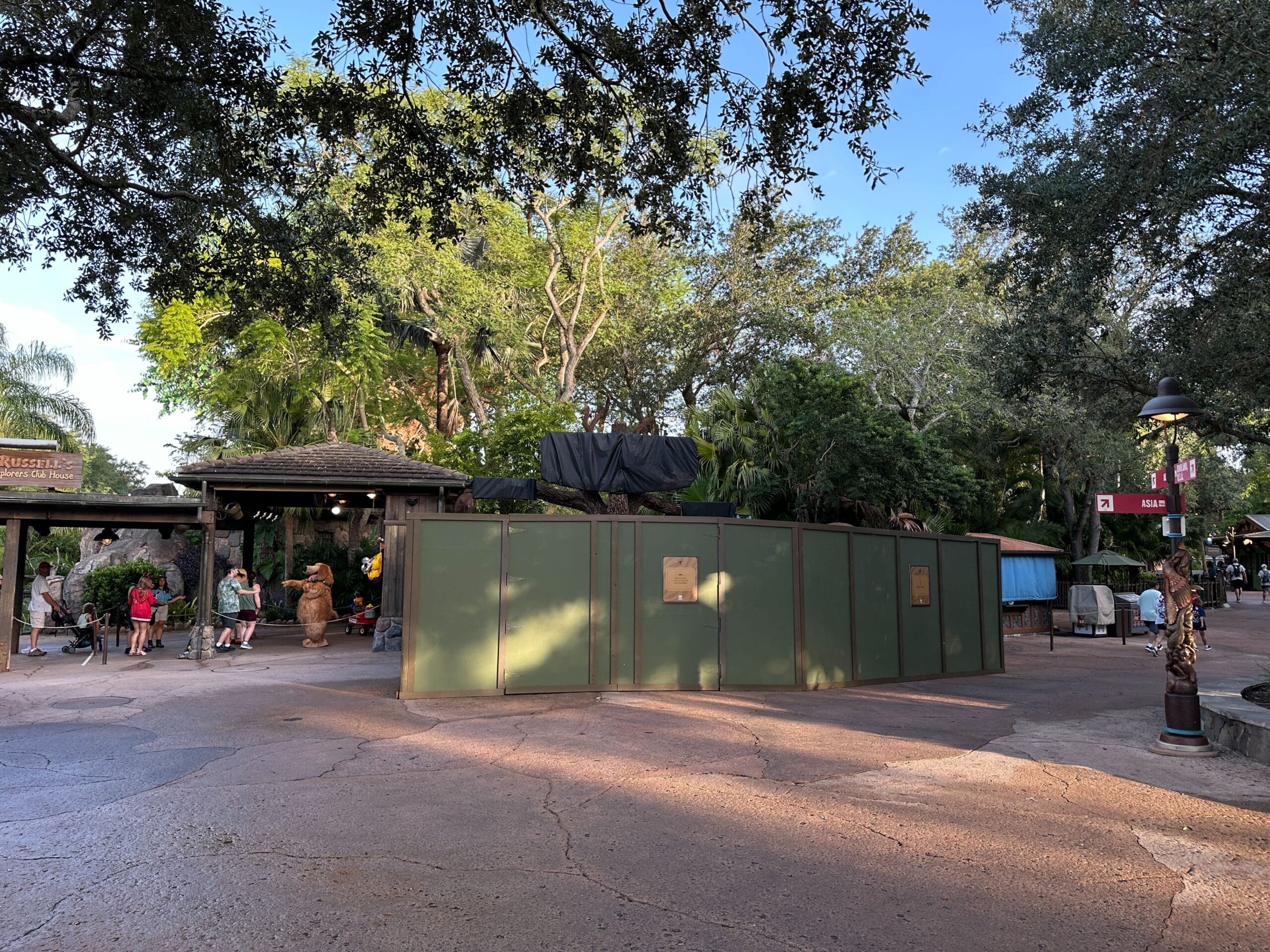 Green construction walls block an area in Animal Kingdom, with trees and people nearby under a clear sky.