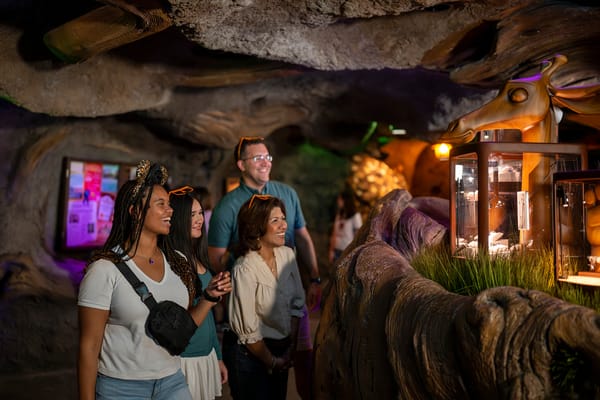 Four guests smile while exploring Zootopia exhibits in a dimly lit, cave-themed Disney attraction, reminiscent of park experiences.