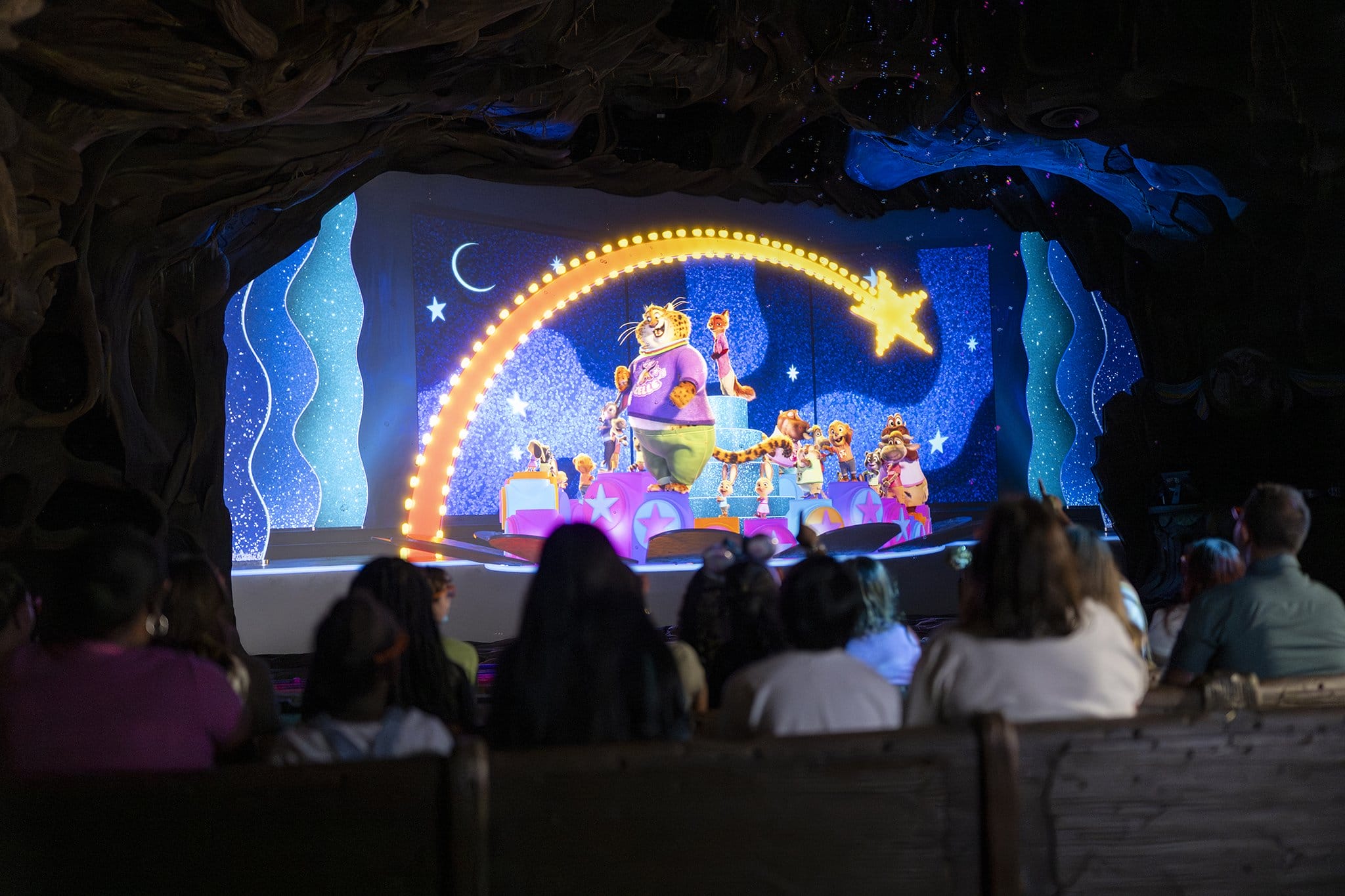 Guests at a Disney park view an animatronic animal performance in a star-lit, Zootopia-themed theater, with no castle in sight.