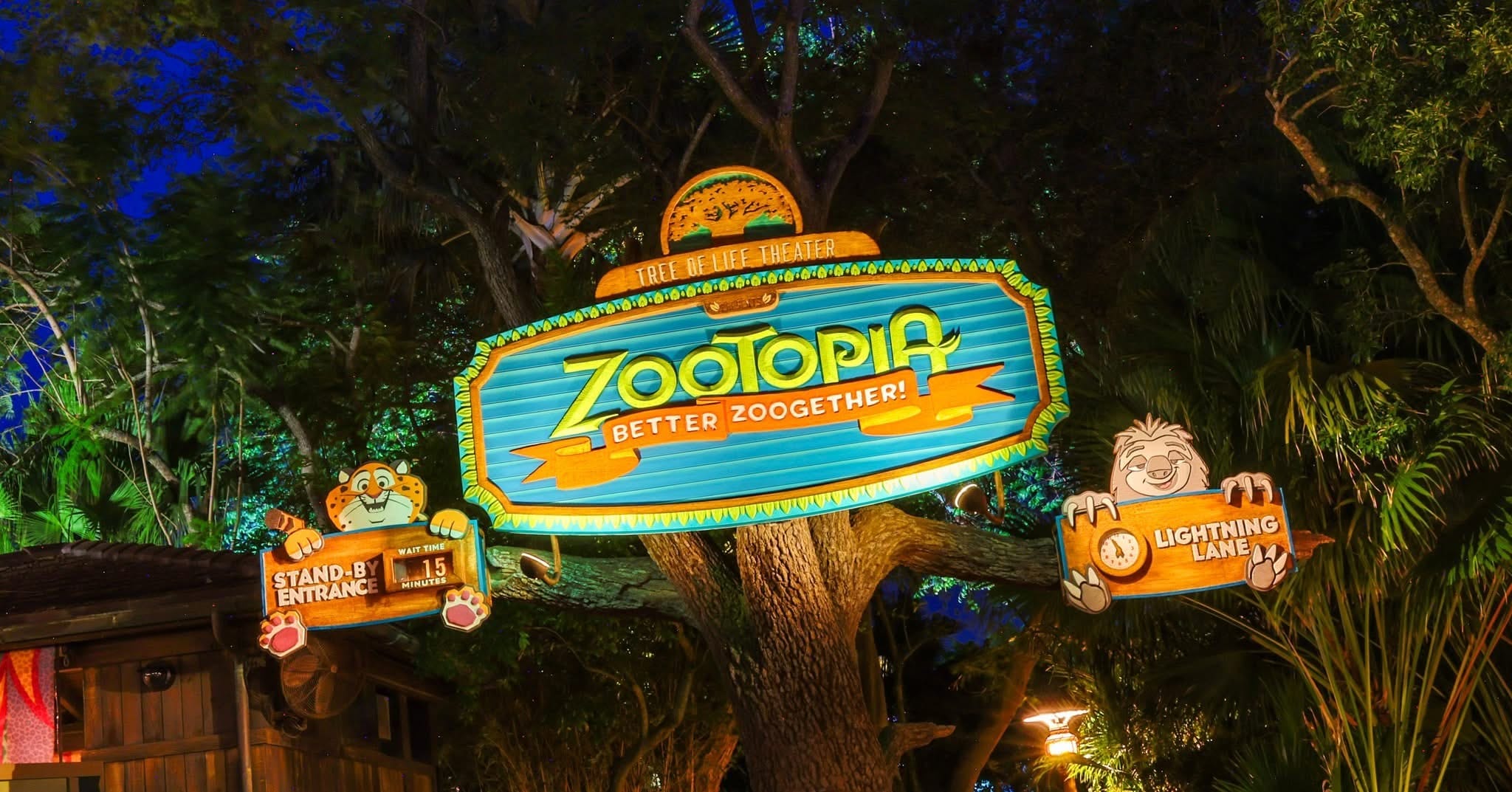 Vibrant "Zootopia: Better Zoogether!" sign glows at a Disney park entrance, encircled by trees, illuminated against the night.