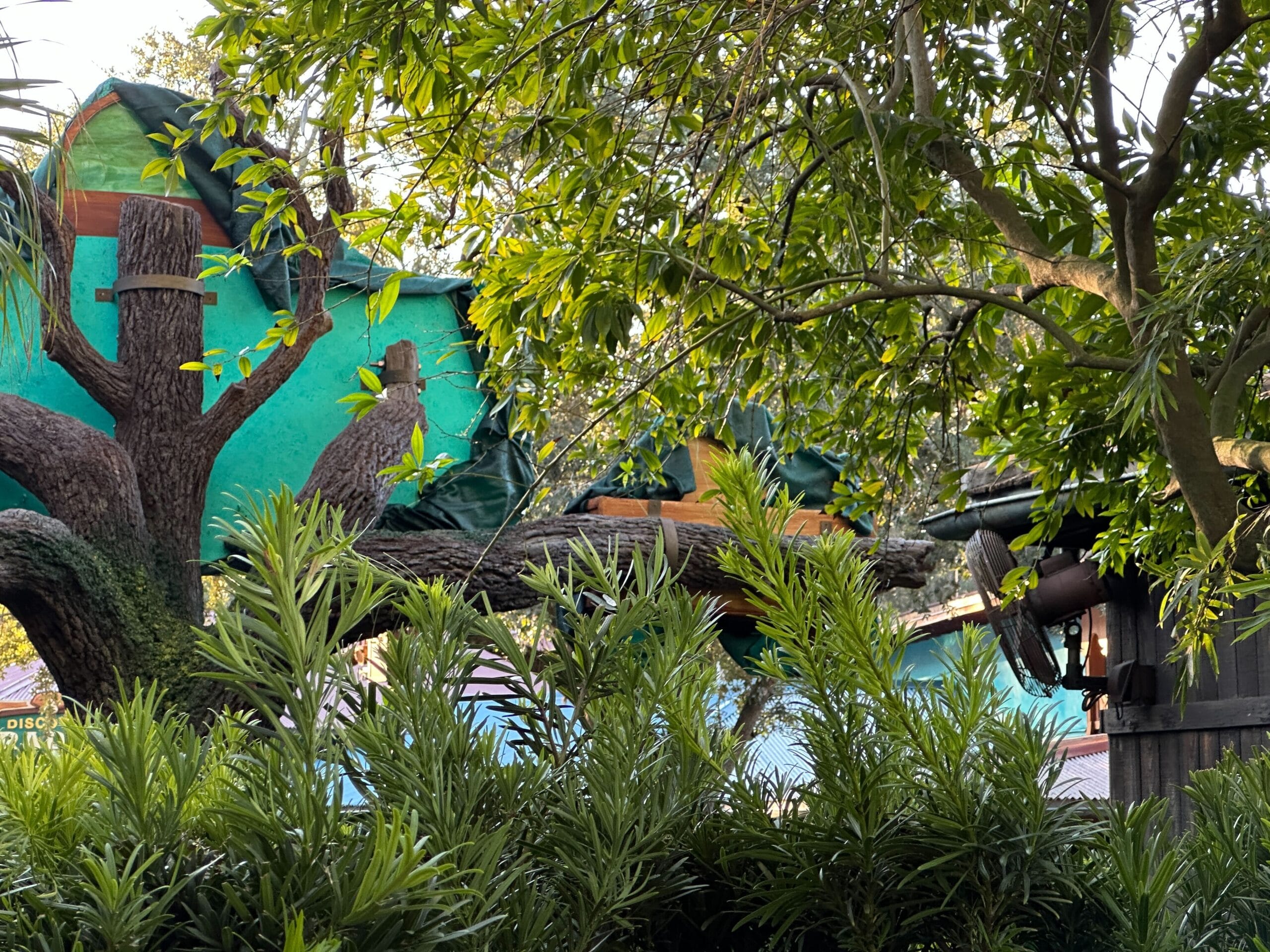 A treehouse with green tarps and dense foliage, resembling an adventure spot in Zootopia’s Animal Kingdom at a Disney park.