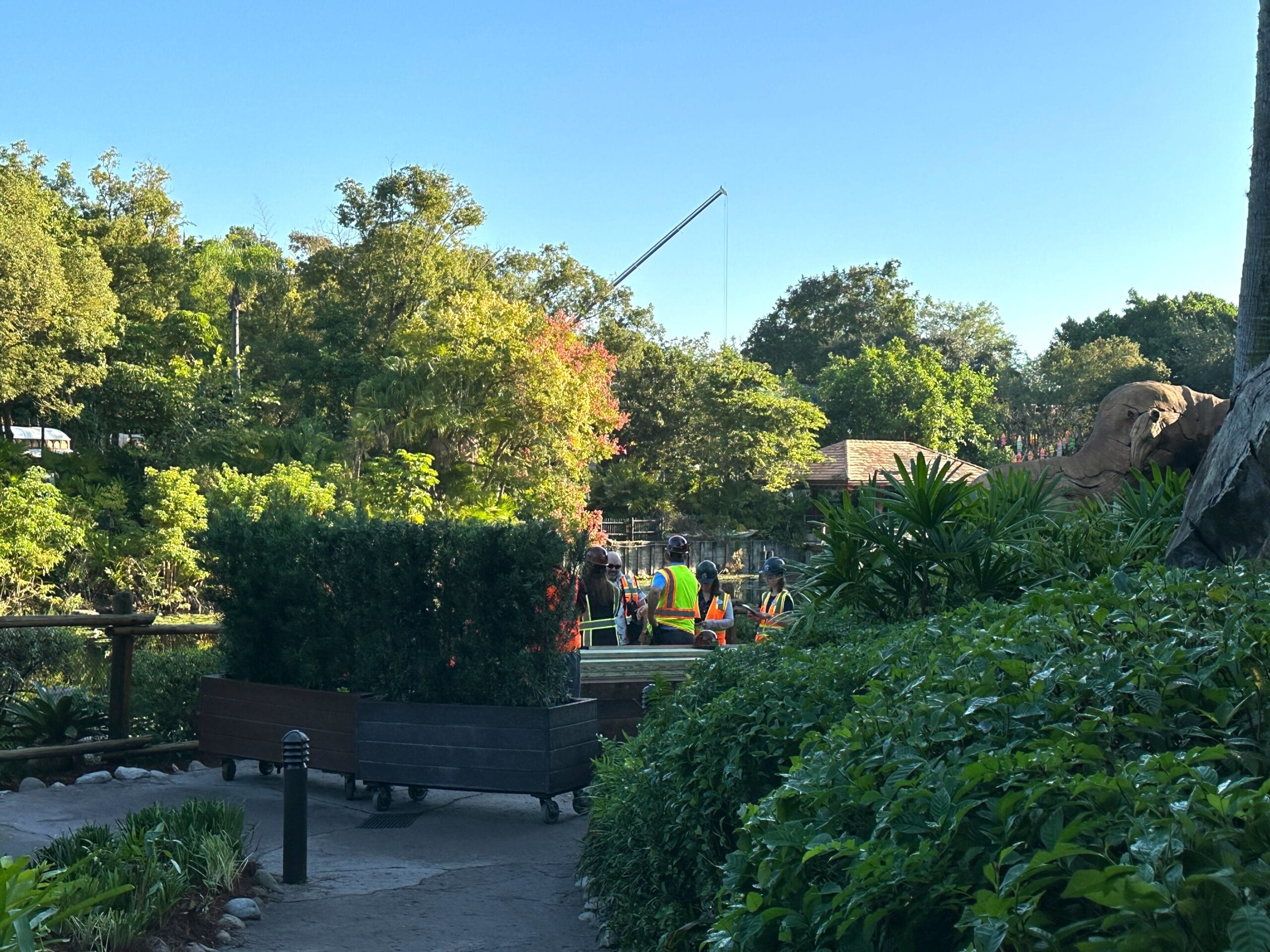 Workers in safety vests by a crane along a river, surrounded by Animal Kingdom’s lush greenery, giving Zootopia construction vibes.