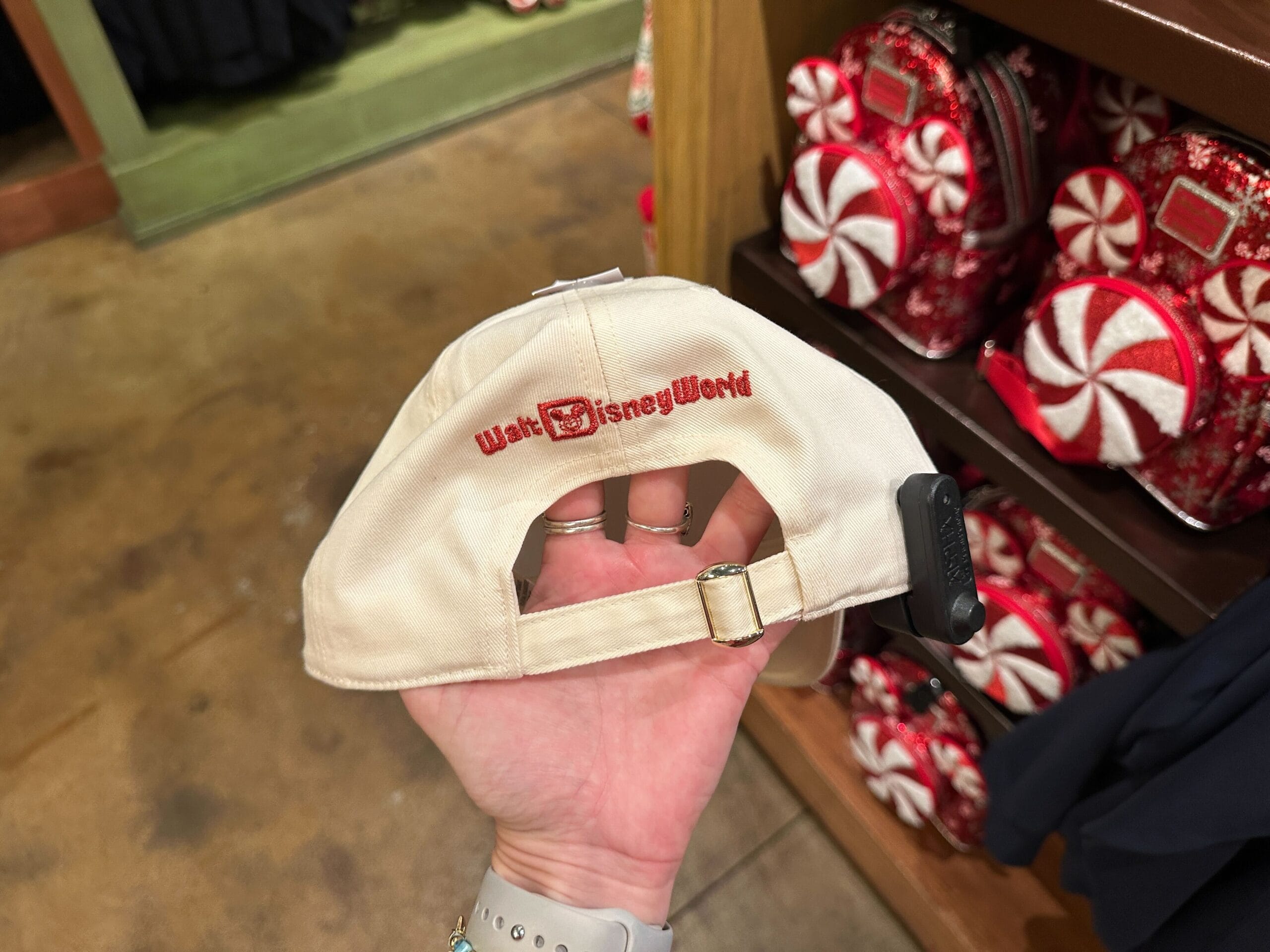 A hand holds a beige Walt Disney World hat near festive red-and-white bags, capturing that classic WDW style over Disneyland’s.
