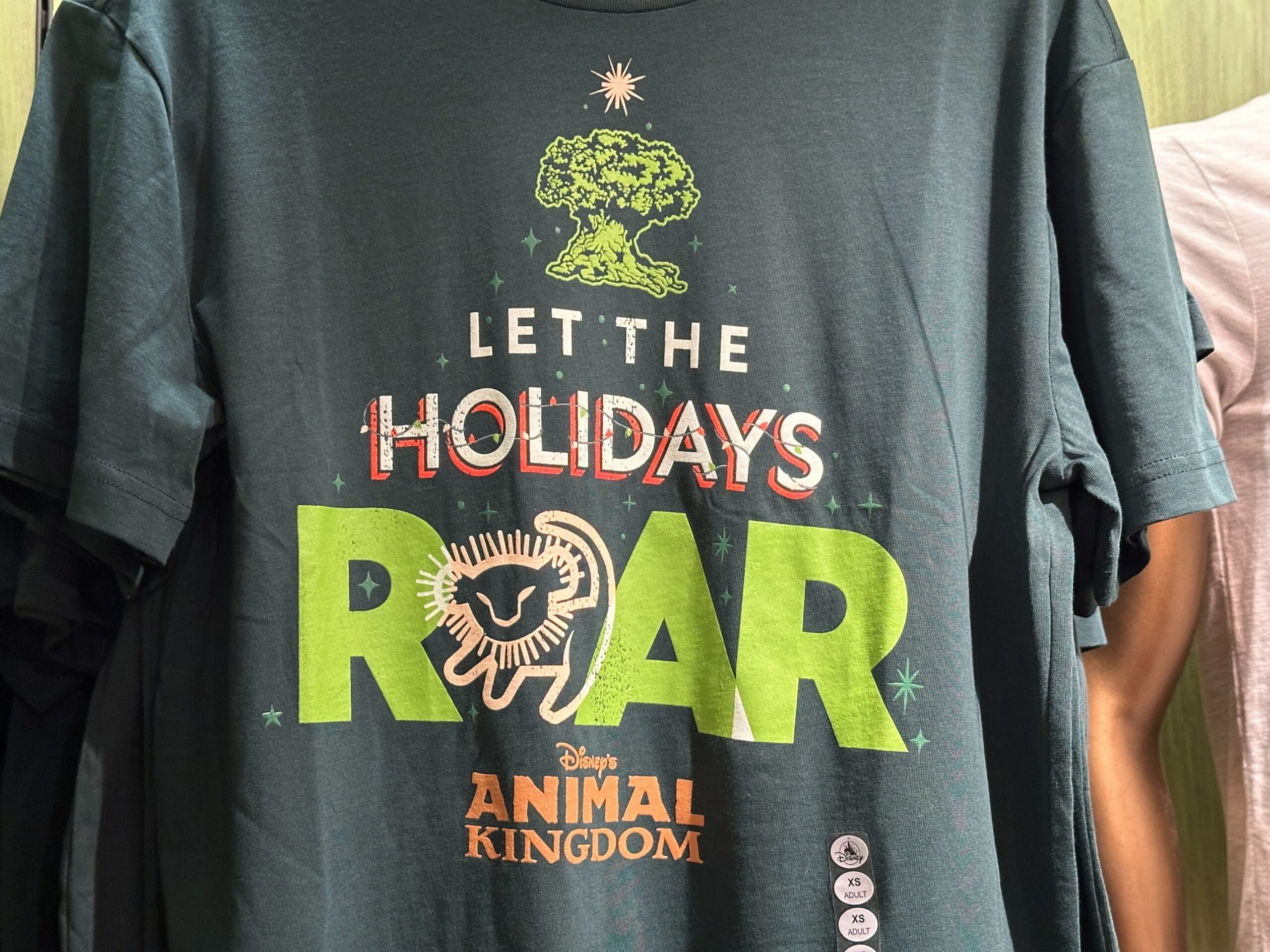 Dark green Holiday Tee featuring Disney’s Animal Kingdom logo, a lion, tree, and "Let the Holidays Roar" festive message.