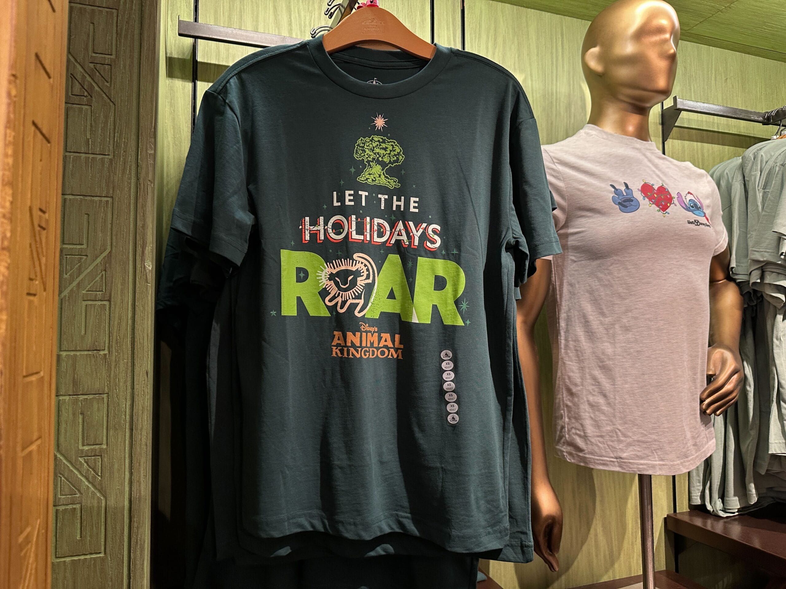 Dark green tee says "Let the Holidays Roar" with Animal Kingdom art, seen at Disney World—not near a castle like Magic Kingdom’s.